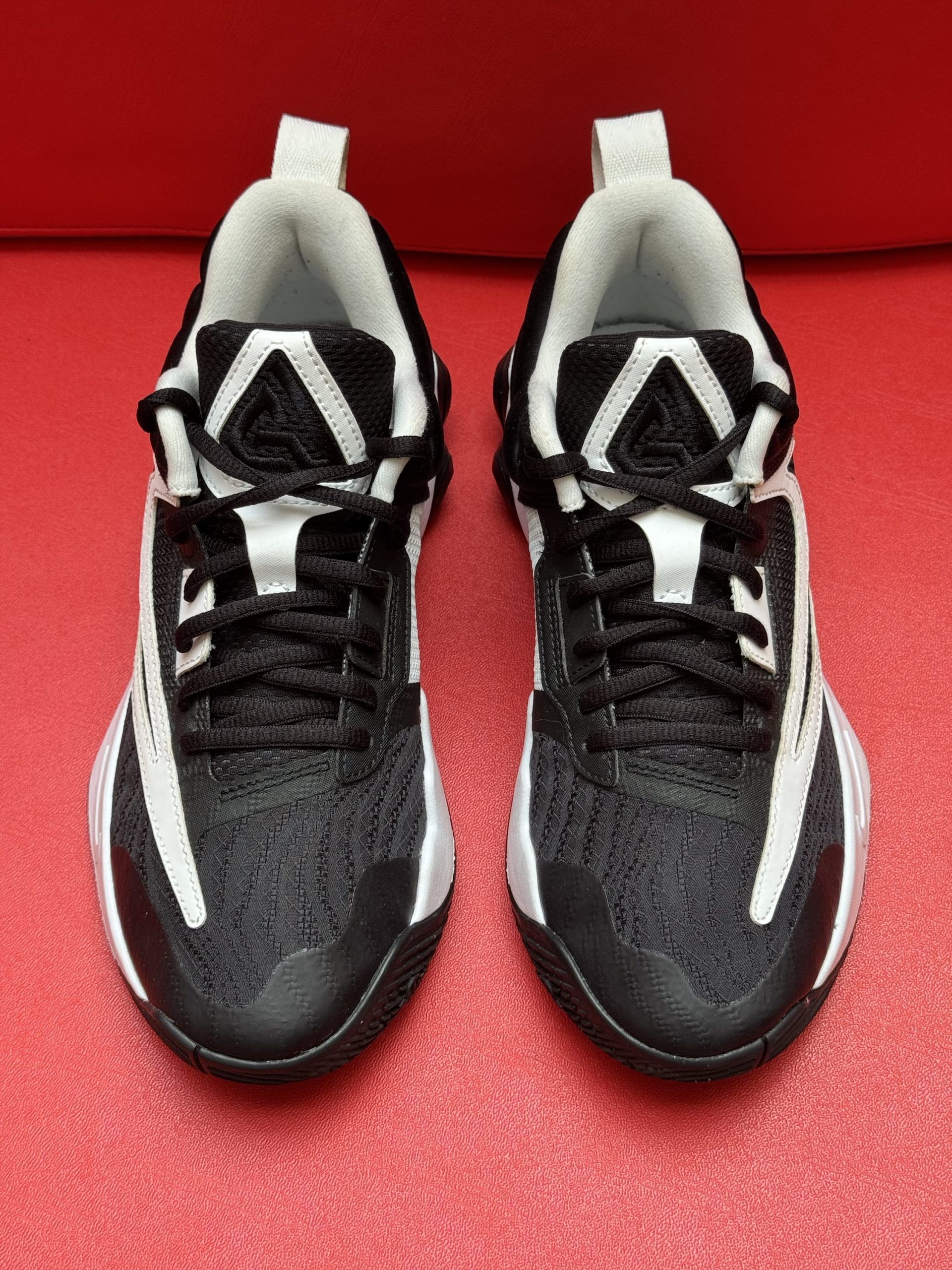 Black and white athletic shoes on a red surface; size 6.5 M.