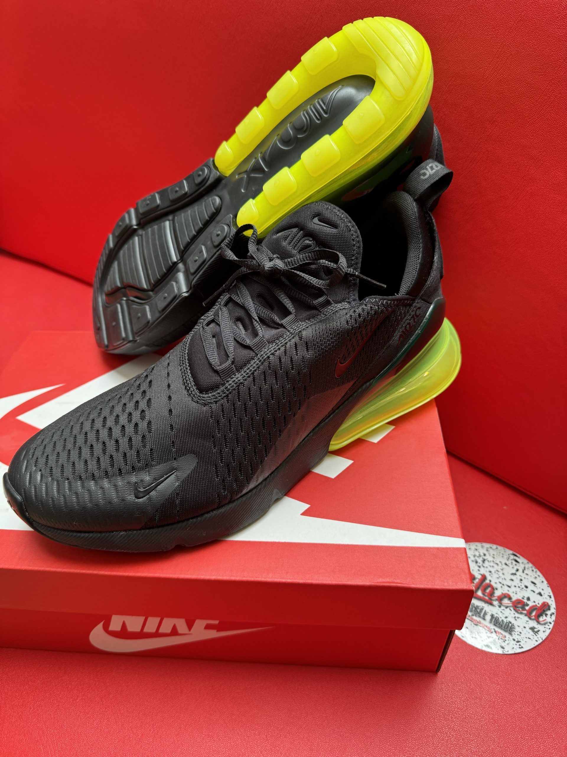 Black and yellow Nike Air Max 270 sneakers atop a red shoe box and surface.