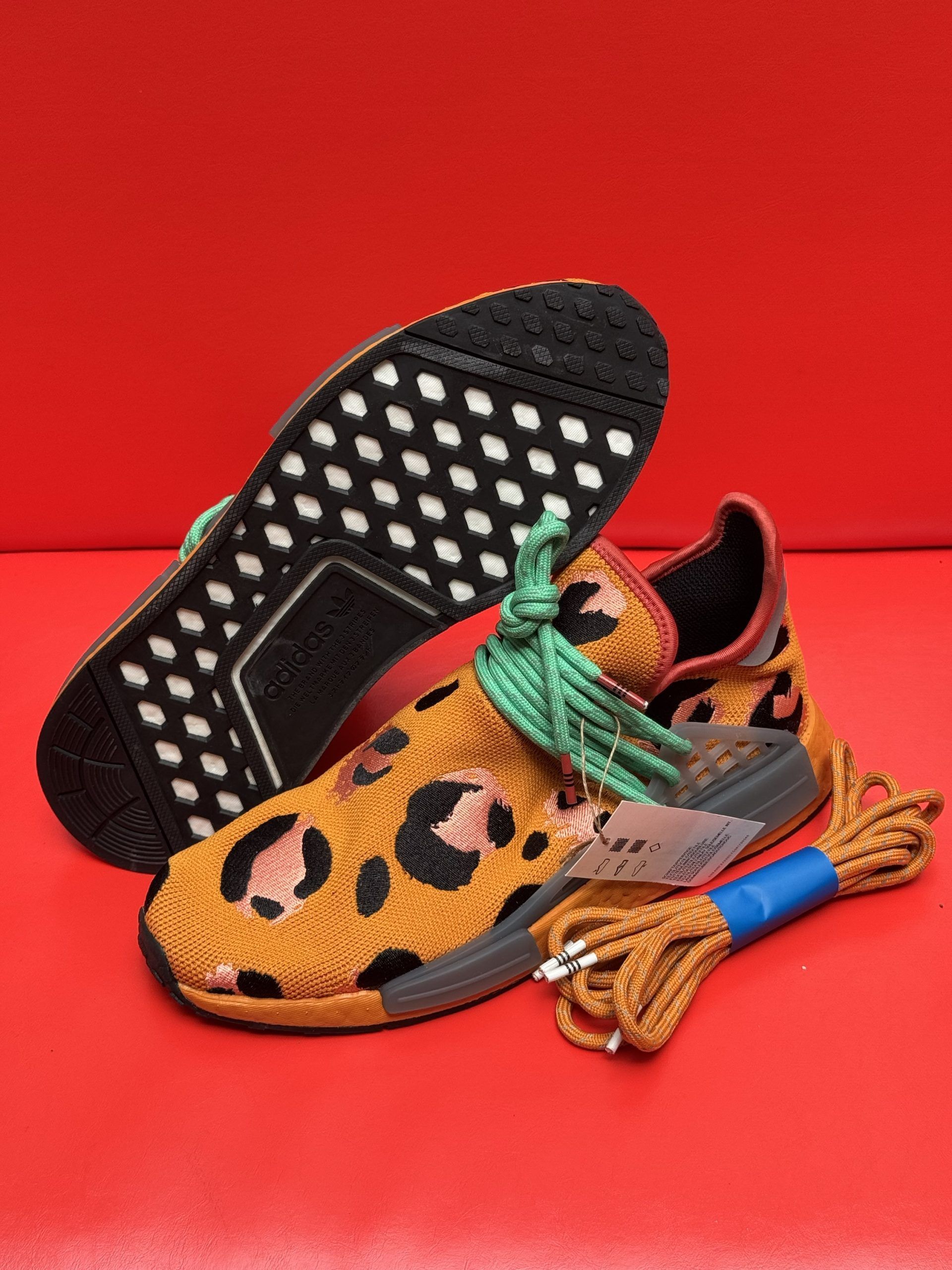 Leopard print sneakers with green and tan laces, on a red background. One shoe sole up.