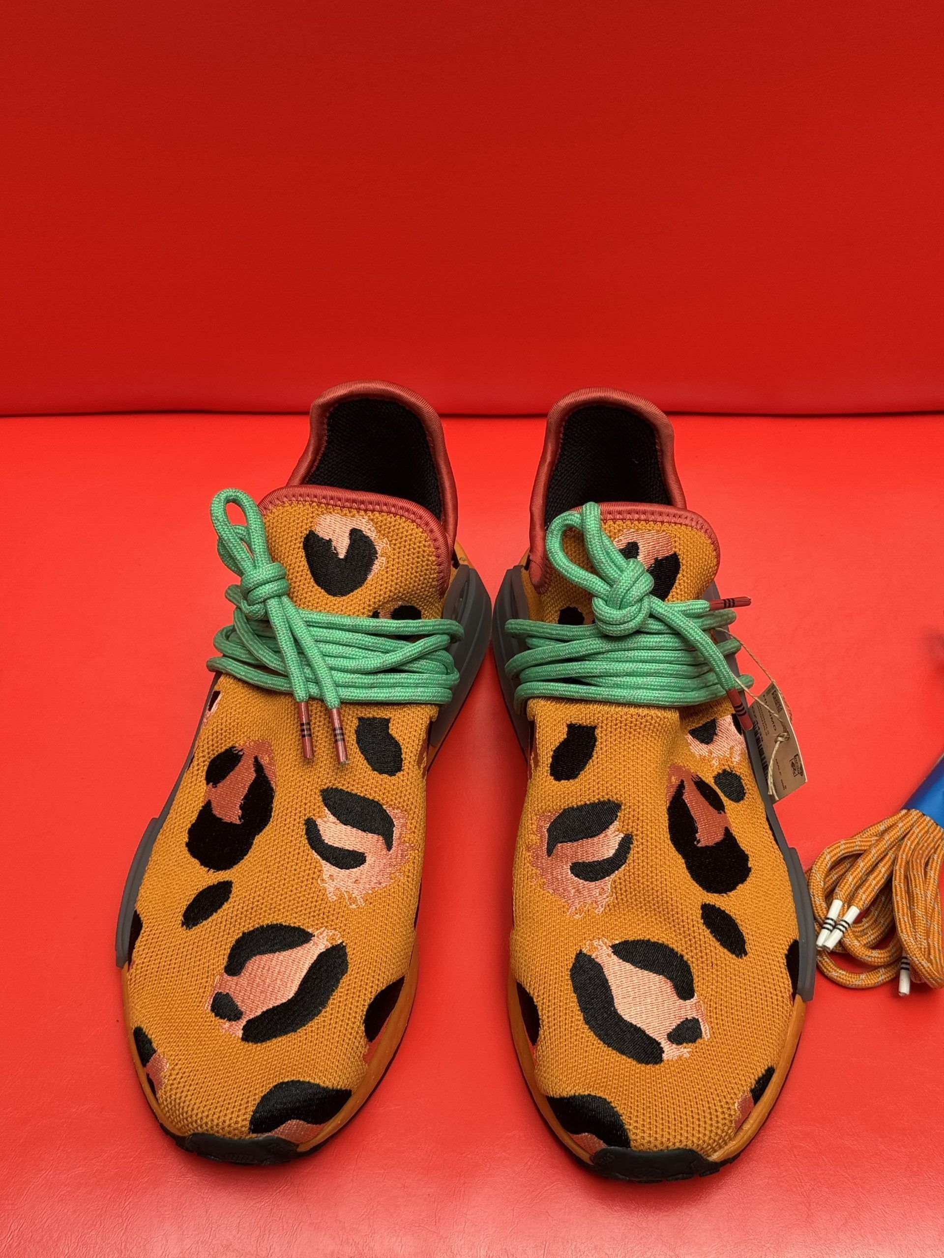 Leopard print sneakers with green and tan laces, on a red background. One shoe sole up.