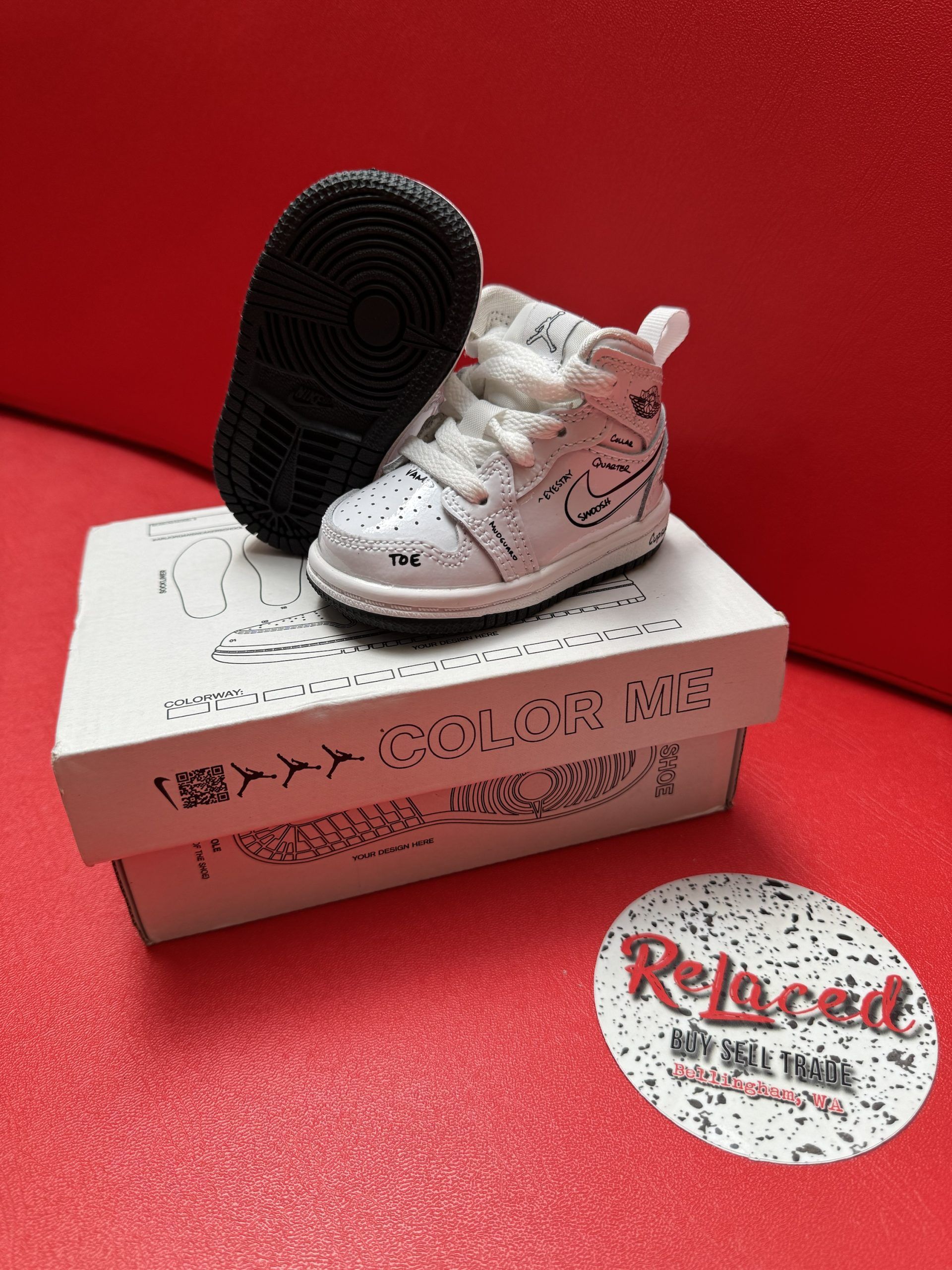 Small white and red baby sneaker with black sole atop a box, red background, with a 