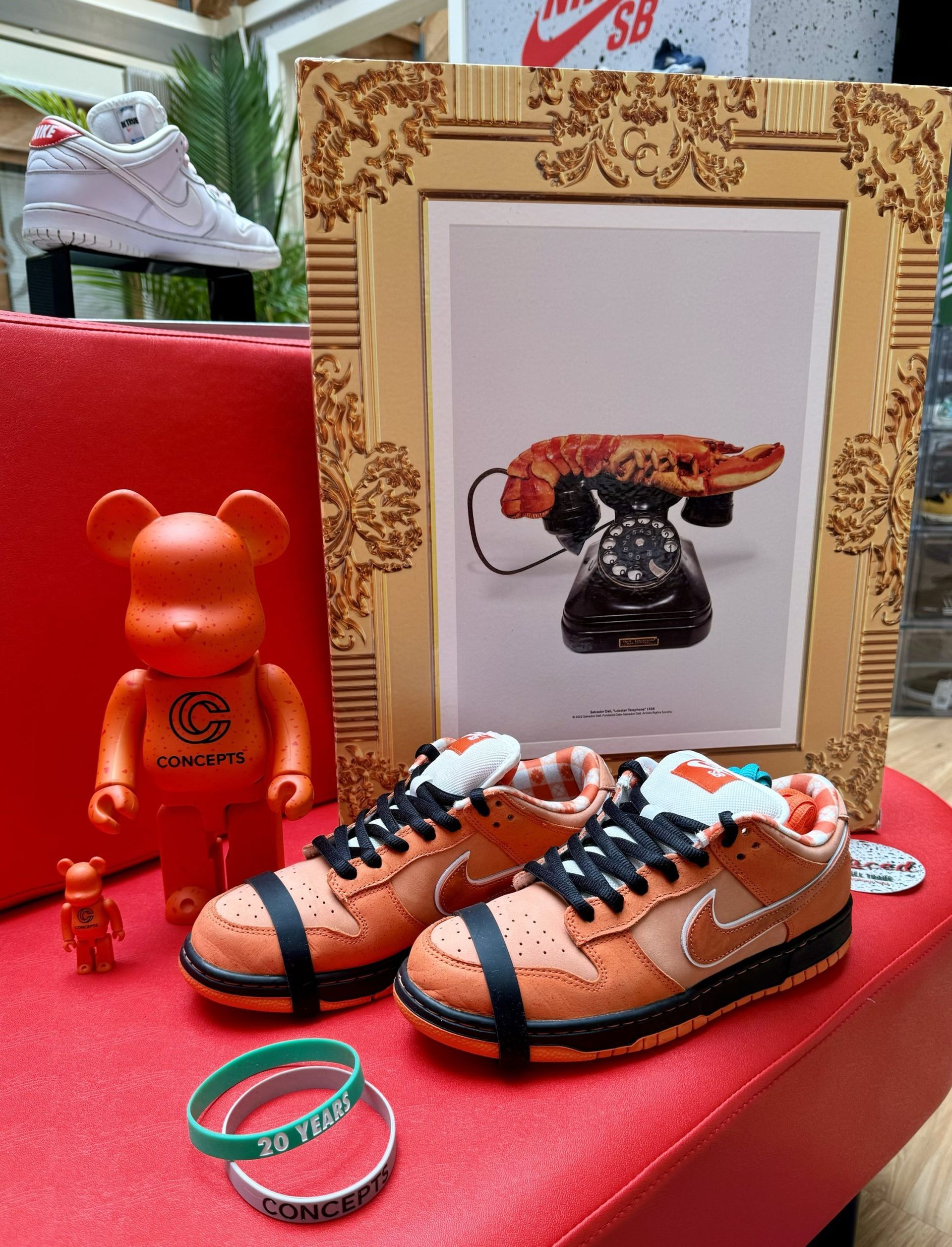 Orange Nike Dunks, artwork of a telephone, orange Bearbricks, and white Nike Air Force 1s on a red surface.