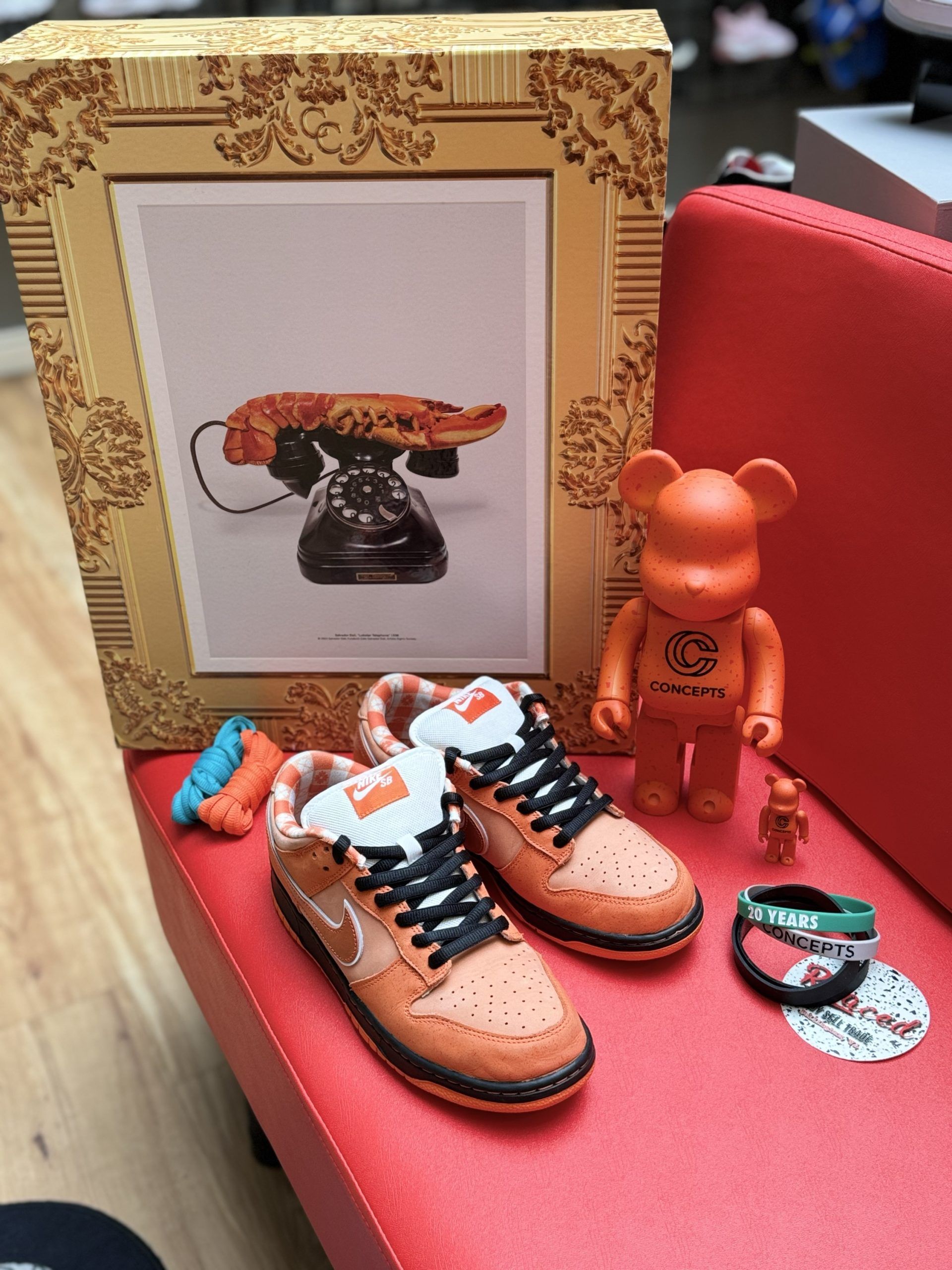 Orange Nike Dunks, artwork of a telephone, orange Bearbricks, and white Nike Air Force 1s on a red surface.