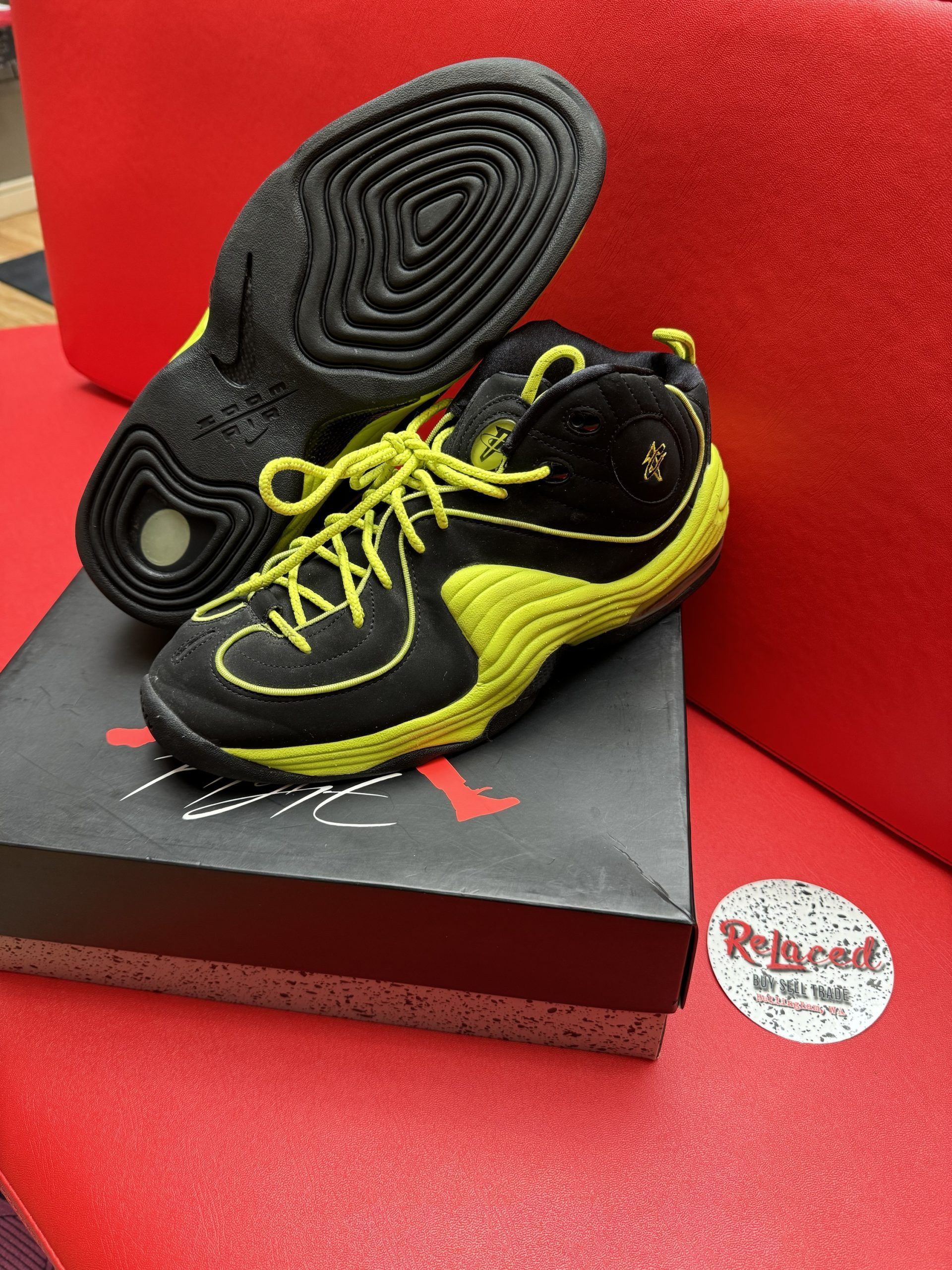 Black and yellow sneakers on a box, sole visible. Red background.