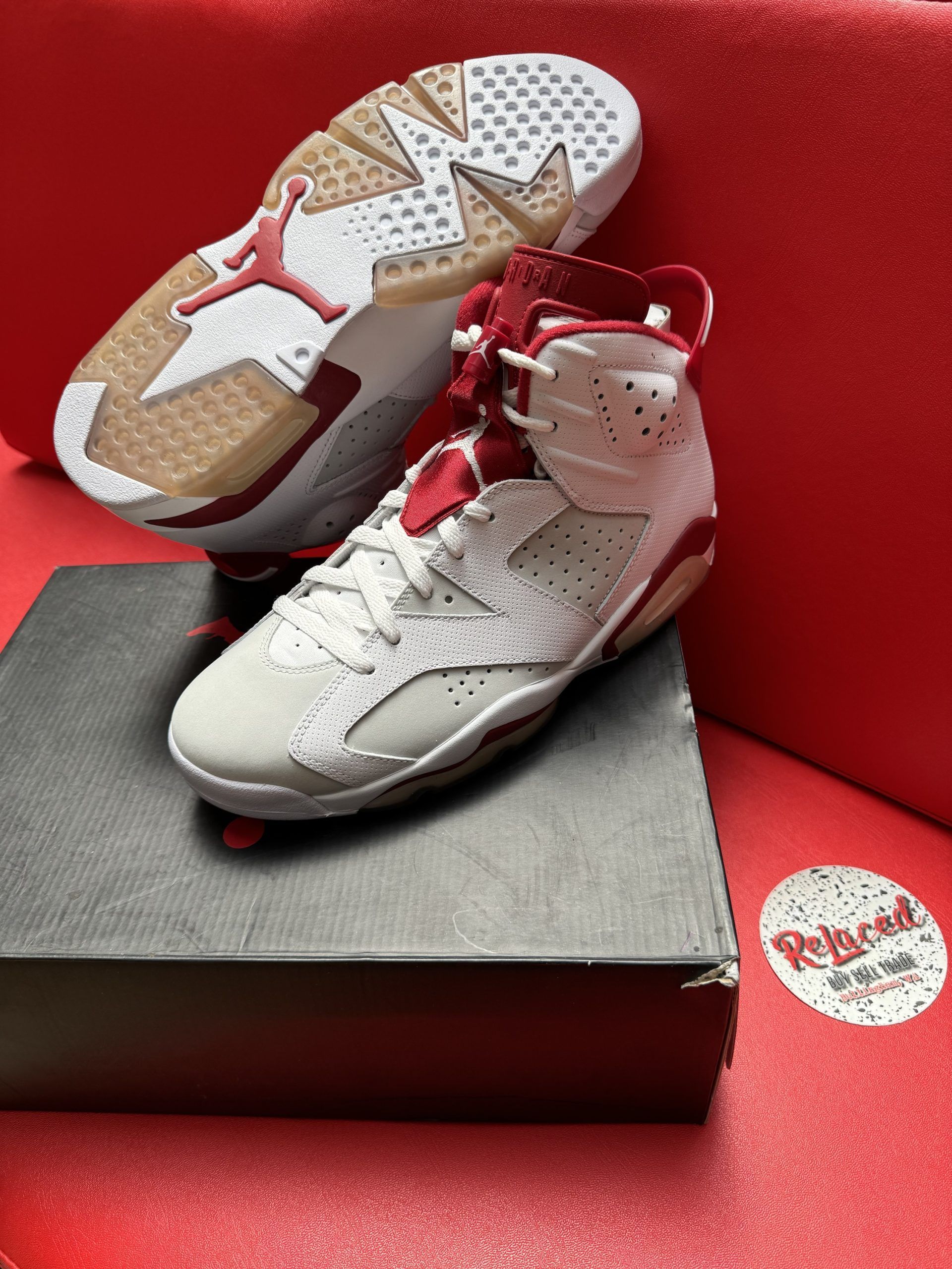 Air Jordan 6 sneakers, white with red accents, on a box, with one sole showing the bottom.