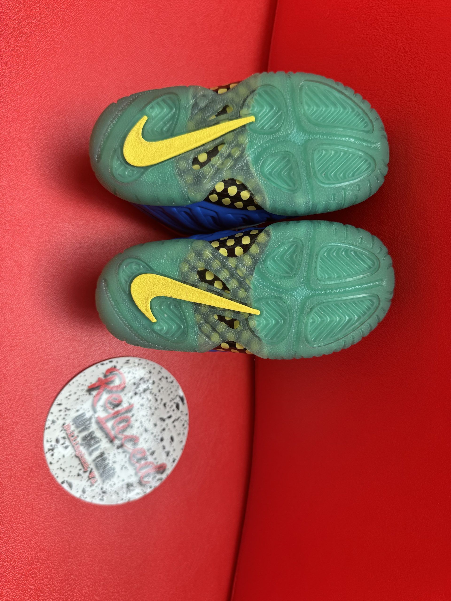 Miniature blue, yellow, and red sneaker with green sole, next to a Relucaed logo, on a red surface.
