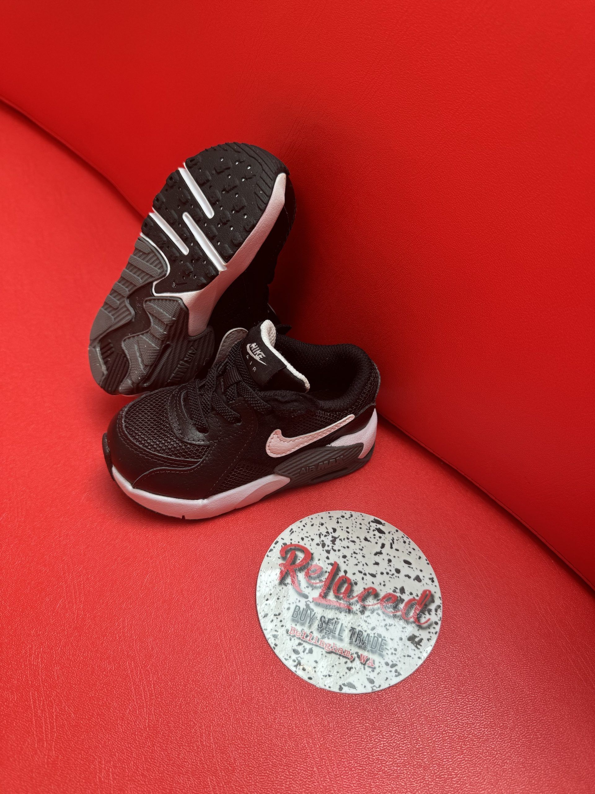 Black and white baby sneakers on red surface next to a round sticker.