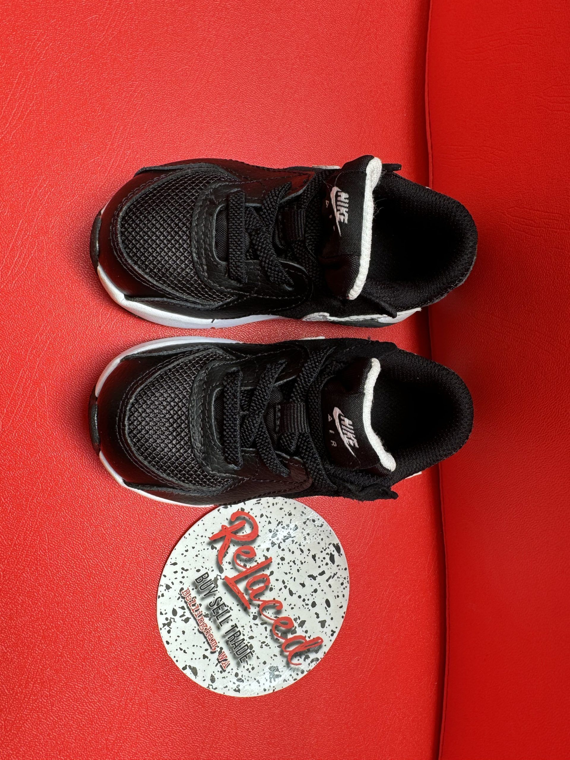 Black and white baby sneakers on red surface next to a round sticker.