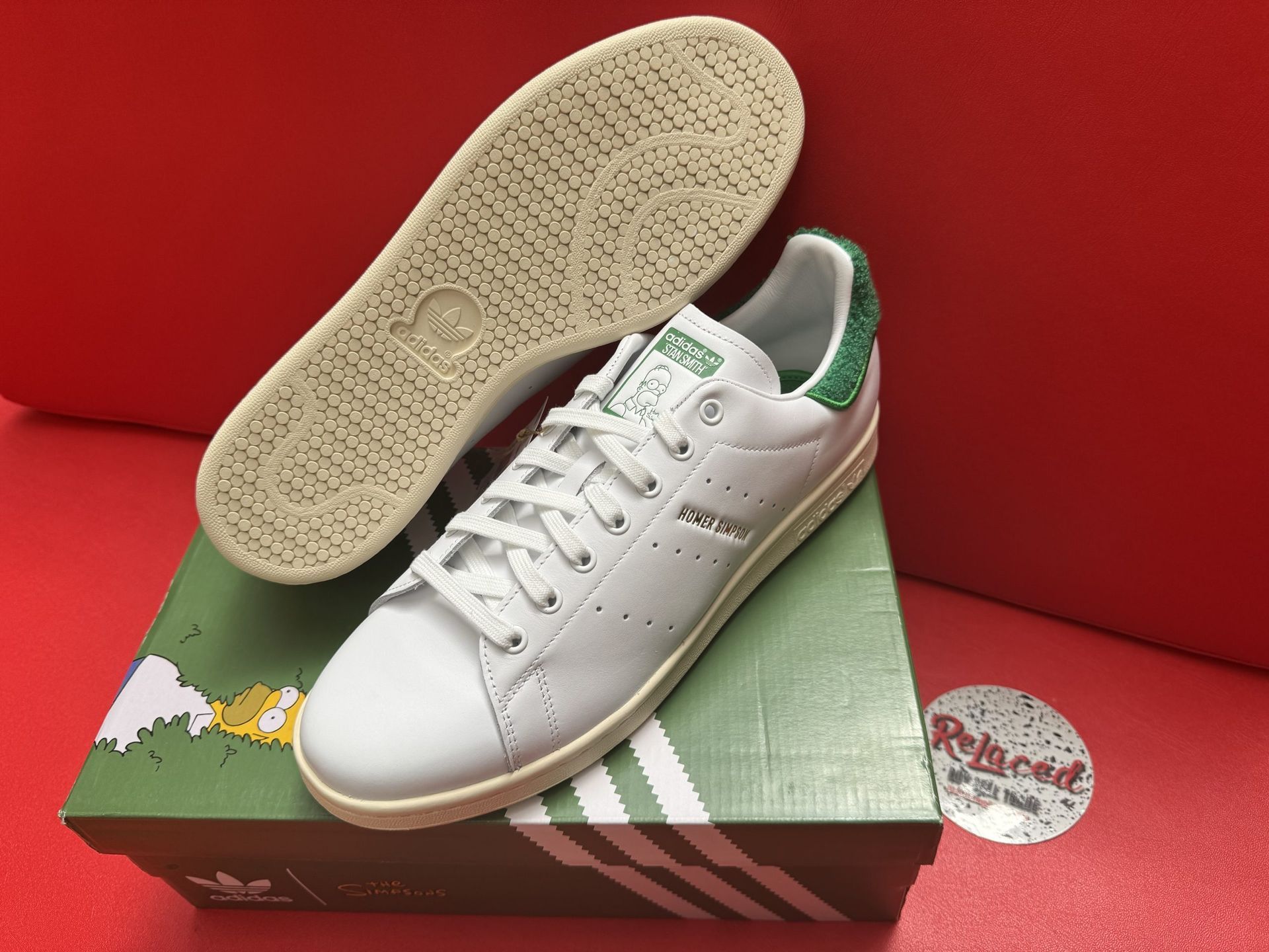 White Adidas Stan Smith sneakers with green accents on a green box and red surface.