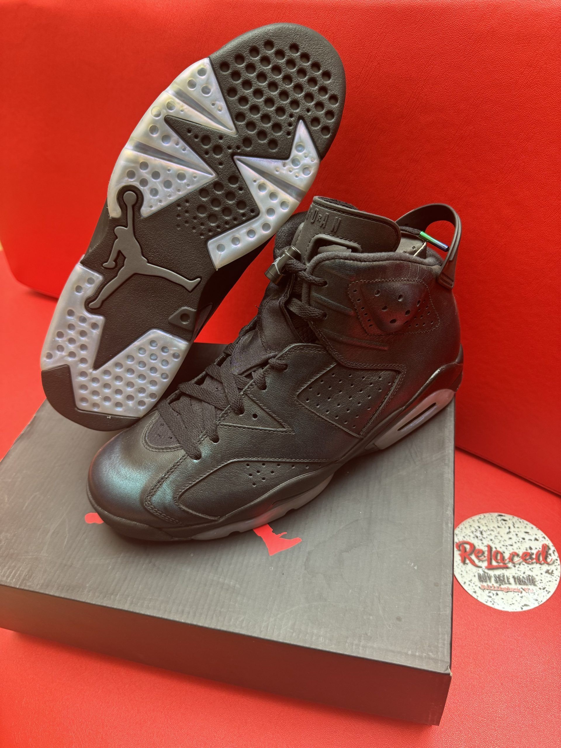 Black and iridescent Air Jordan 6 sneakers on a box, with a clear sole, against a red background.