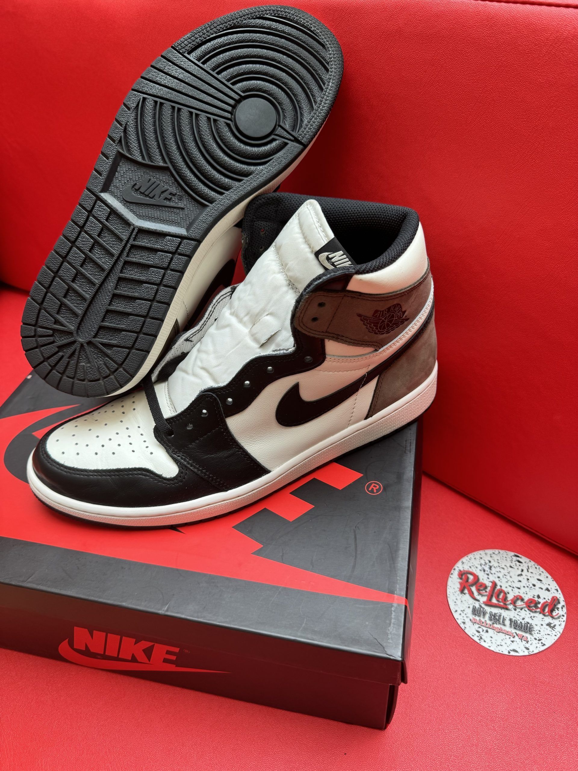 Air Jordan 1 sneakers with black and brown panels, on a box, with a red background.