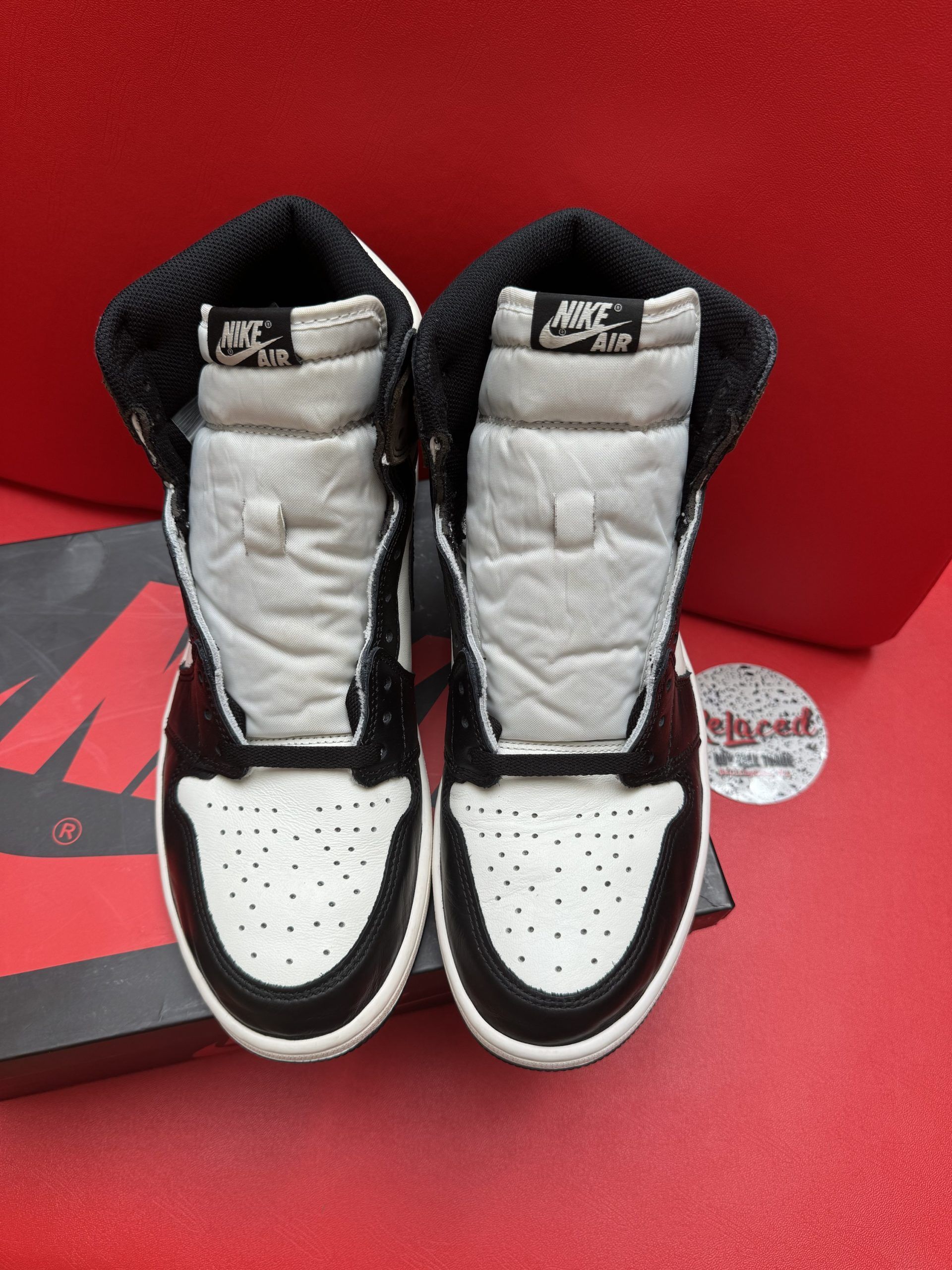 Air Jordan 1 sneakers with black and brown panels, on a box, with a red background.