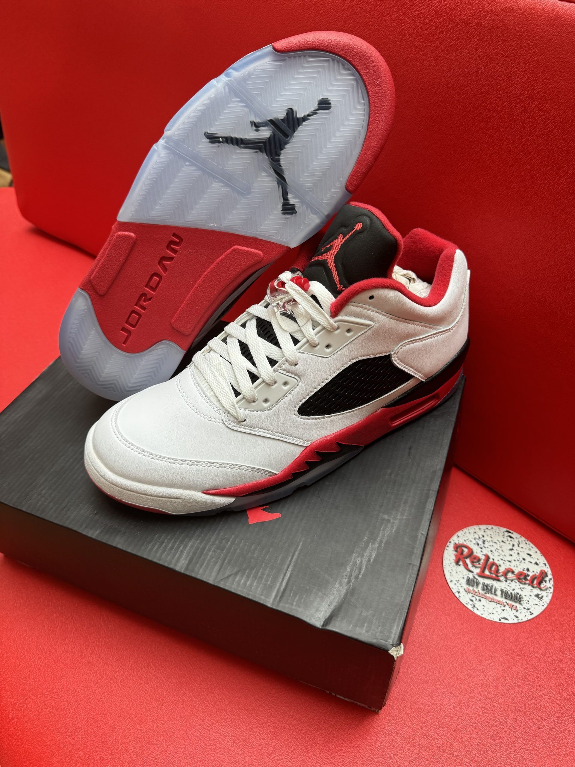 White, red, and black Air Jordan 5 sneakers with a visible sole, sitting on a shoebox.