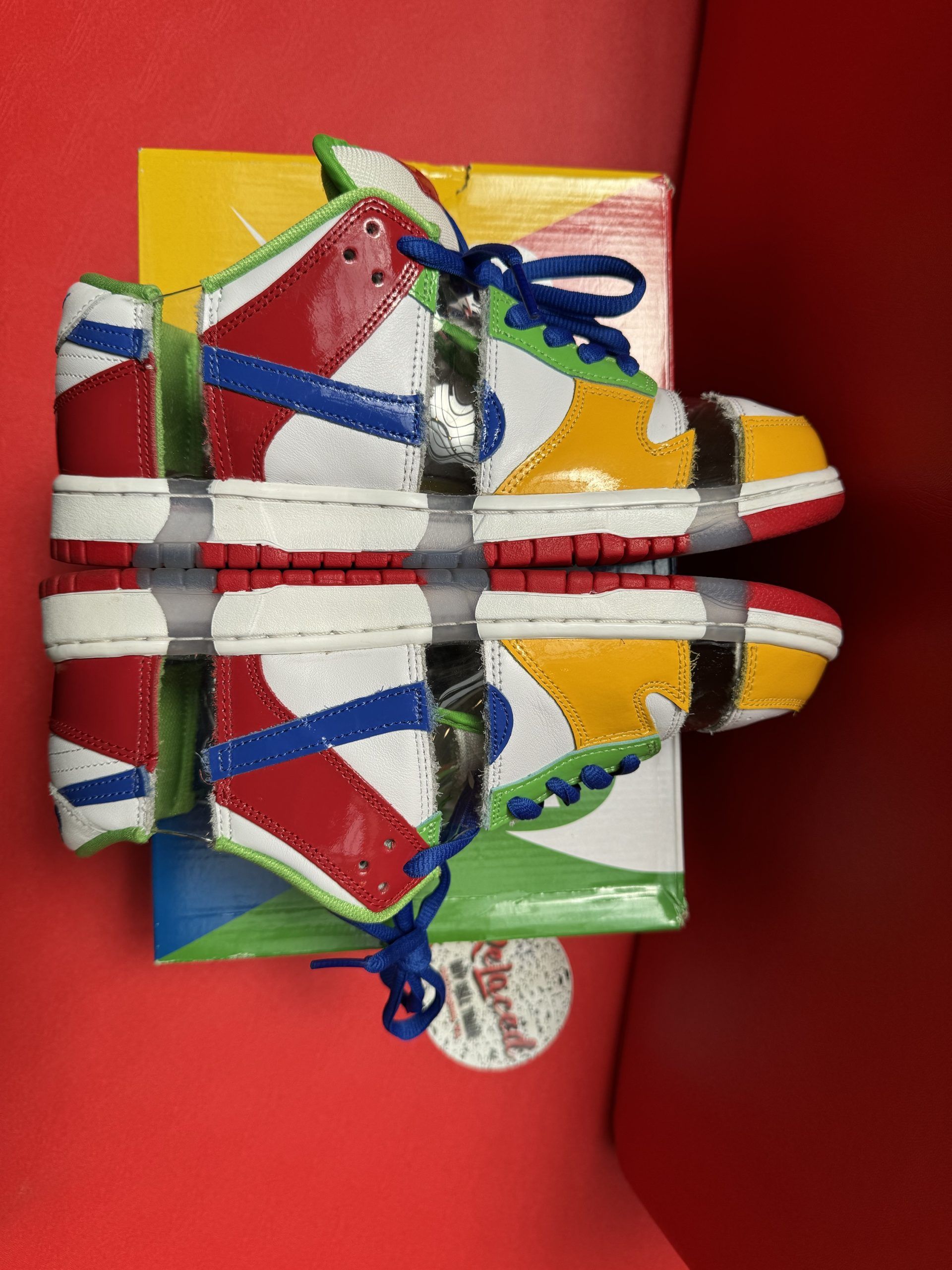 Nike Dunk Low SB sneakers, multi-colored patchwork design, sitting on box, red sole visible, red background.