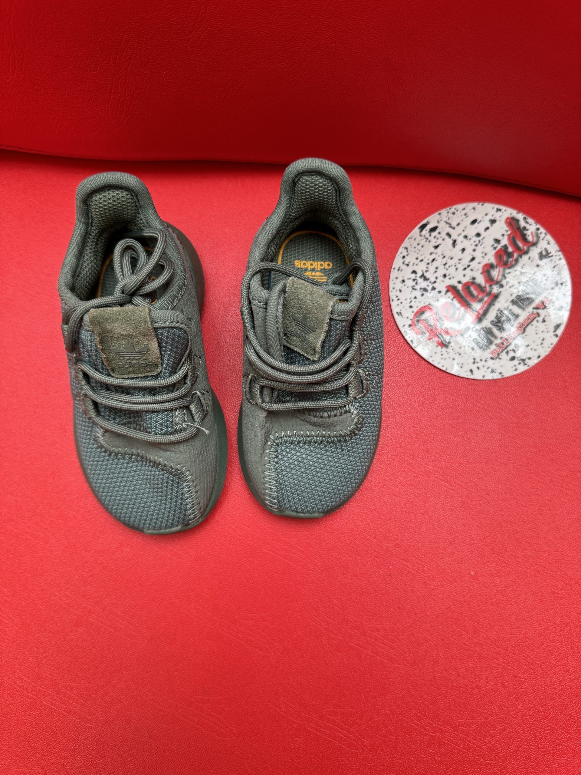 Small gray Adidas shoe on red surface next to a circular sticker that reads 