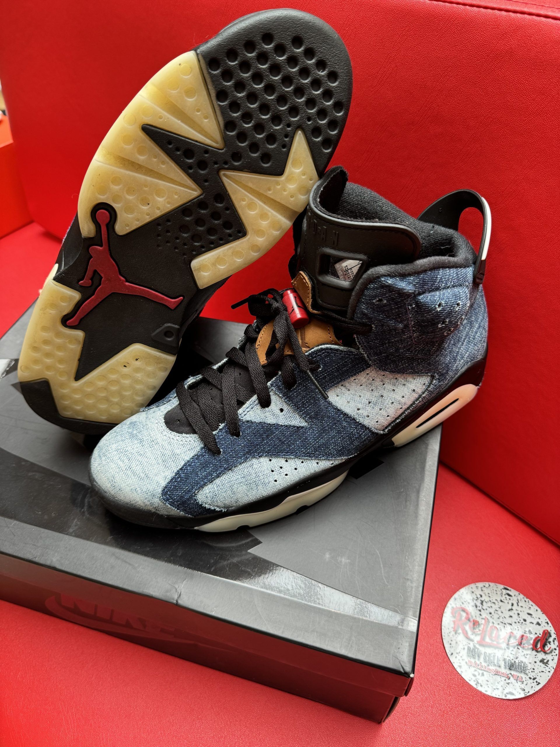 Baby blue and black Air Jordan 6 sneakers, one sole up, on a shoebox. Red background.