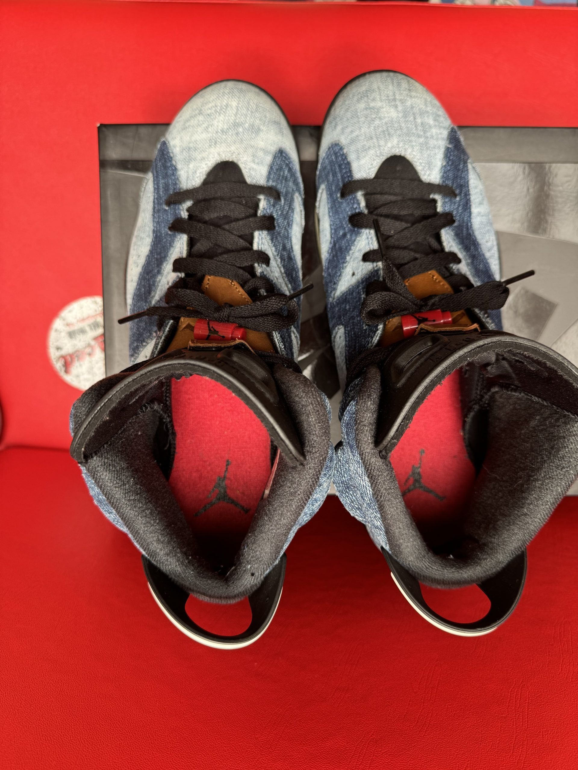 Baby blue and black Air Jordan 6 sneakers, one sole up, on a shoebox. Red background.