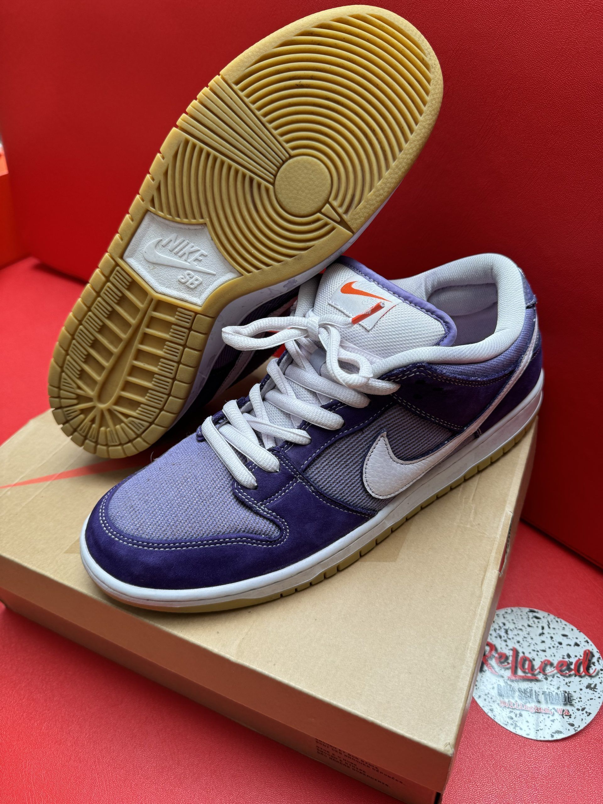Nike Dunk Low SB sneakers, purple, white, and tan. One shoe is upside down, showing sole. On a box.