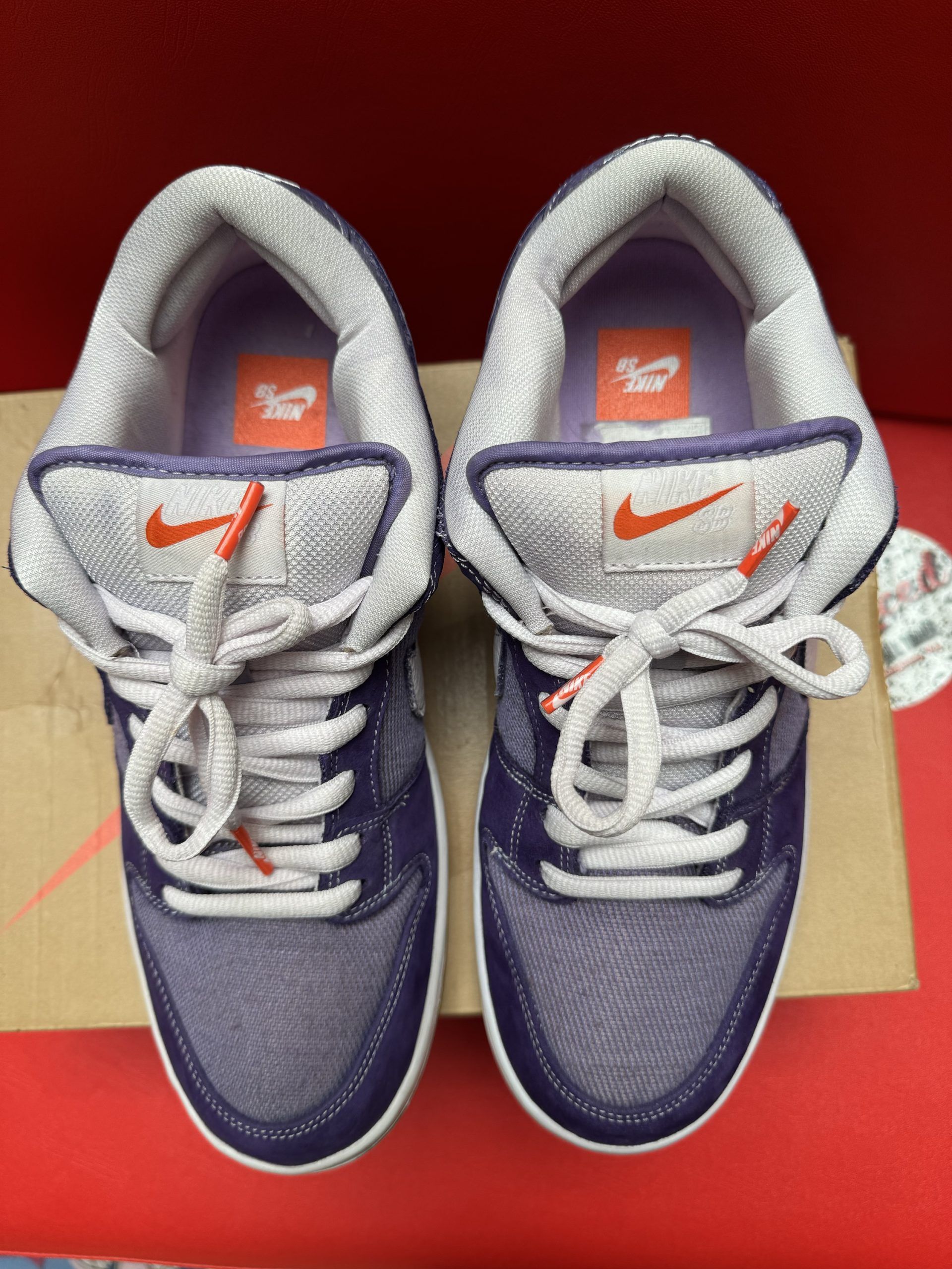Nike Dunk Low SB sneakers, purple, white, and tan. One shoe is upside down, showing sole. On a box.