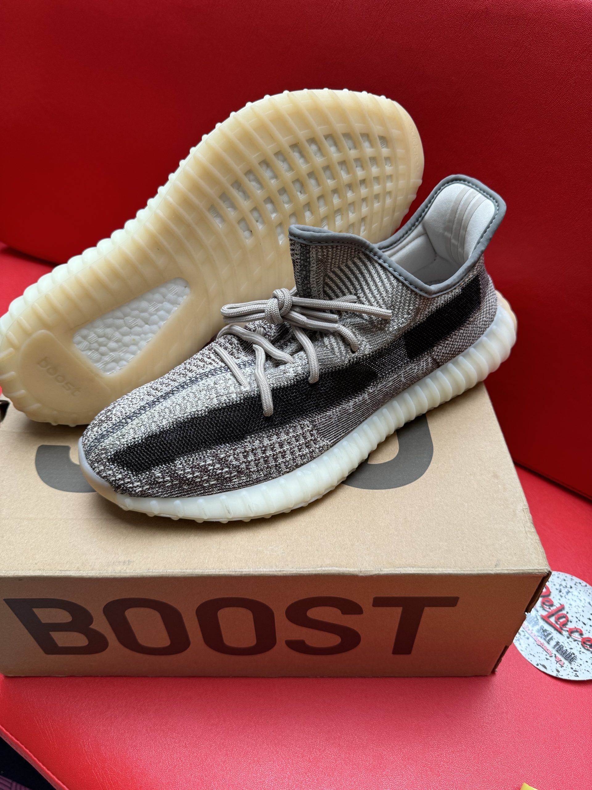 Pair of Adidas Yeezy Boost 350 V1 sneakers, brown and black pattern, on a box, red surface.