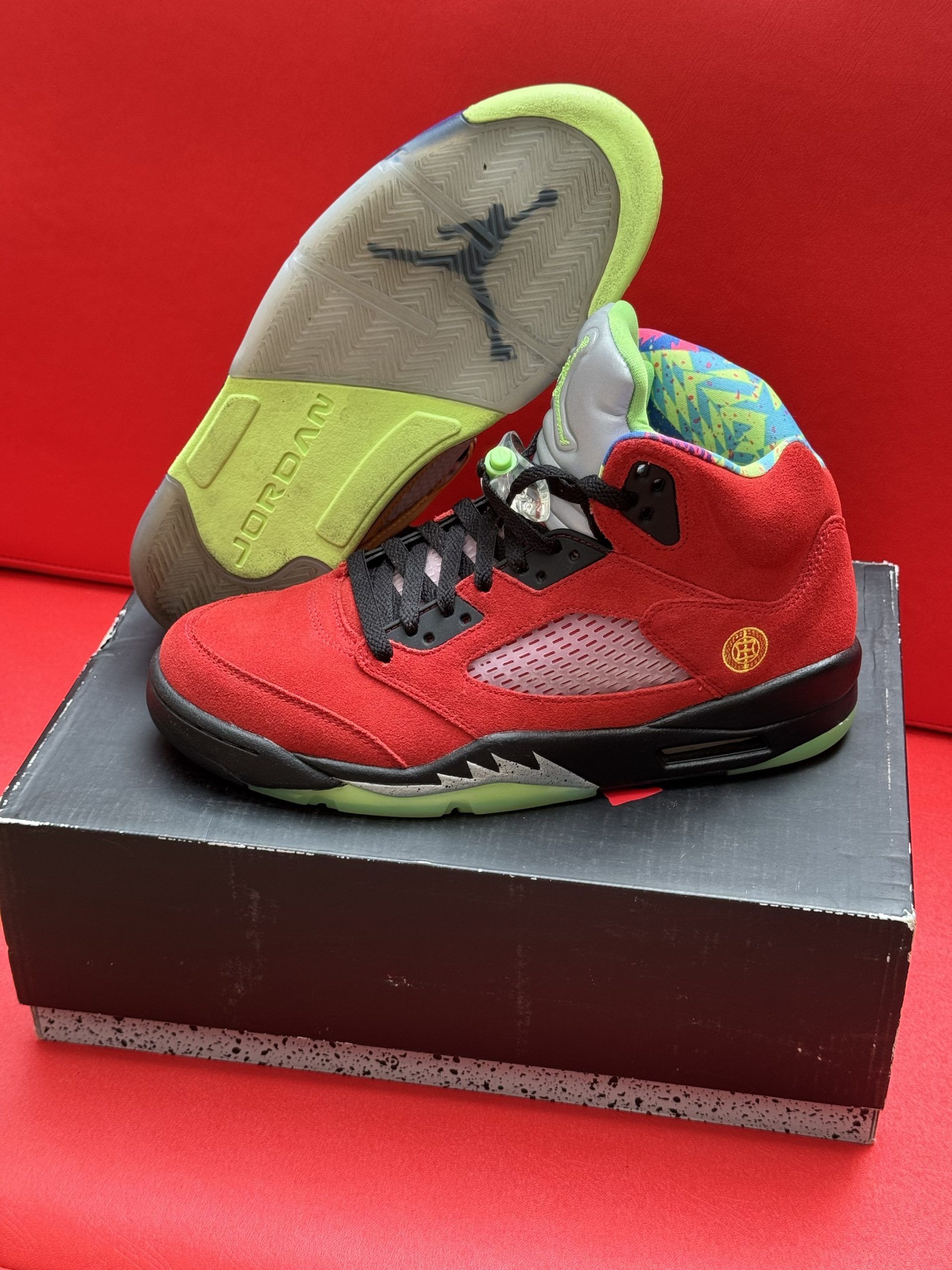 Red and black Air Jordan 5 sneakers with a patterned collar, resting on a shoebox, with the insole visible.