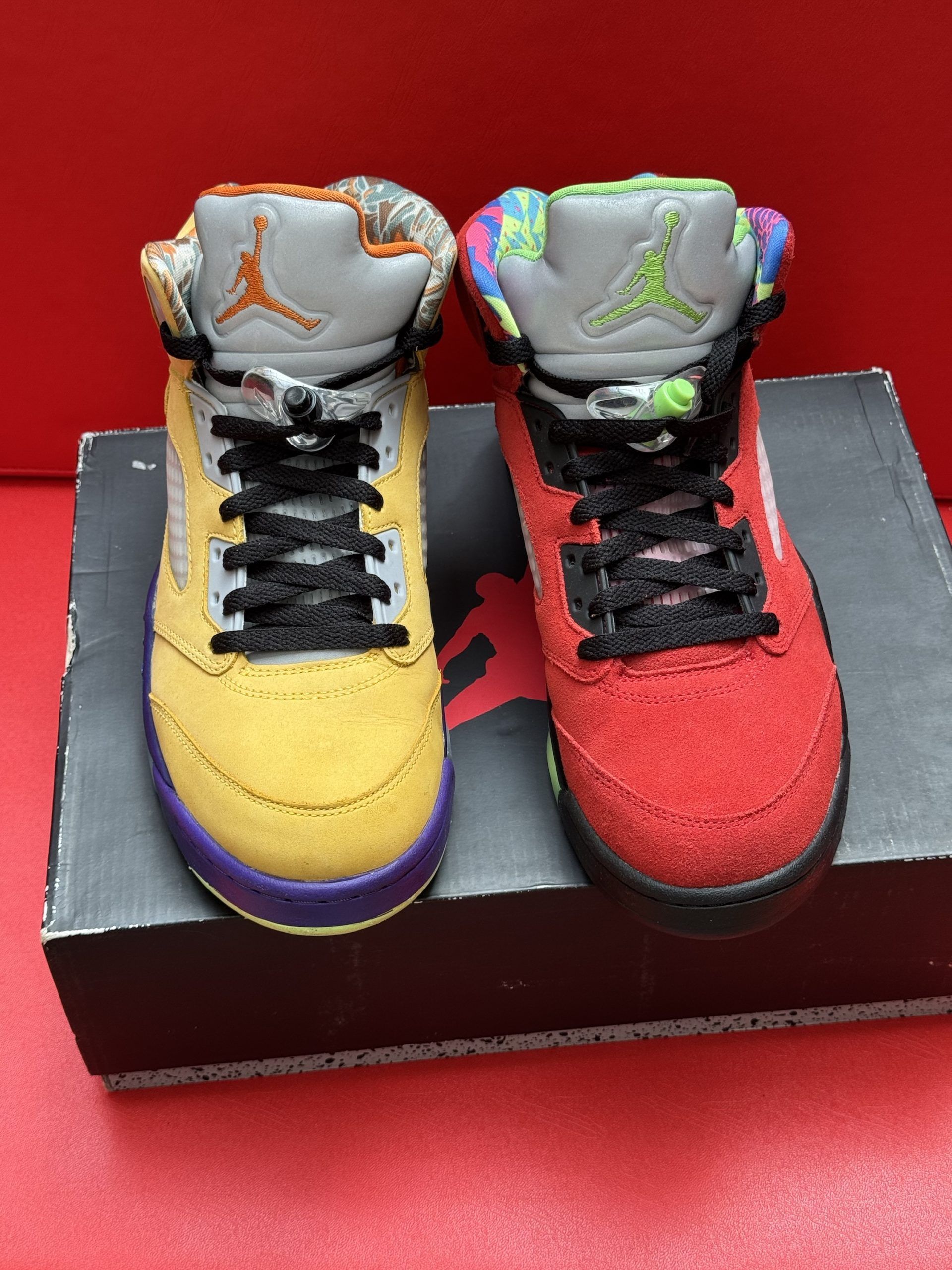 Red and black Air Jordan 5 sneakers with a patterned collar, resting on a shoebox, with the insole visible.