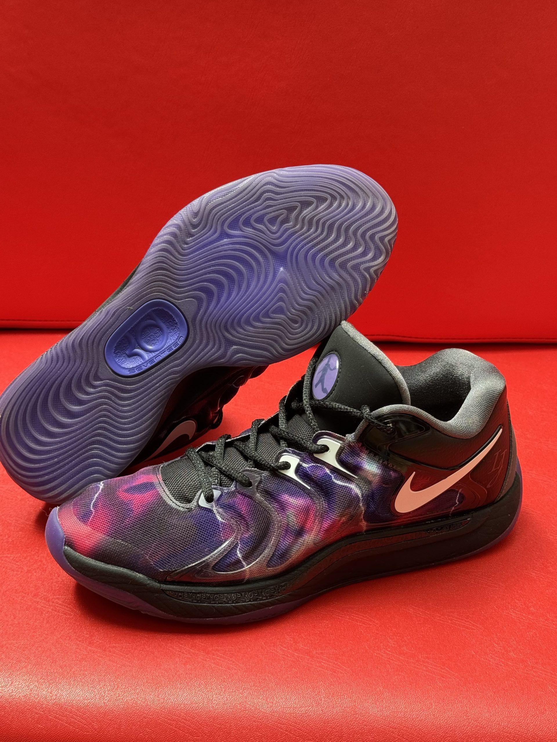 Black and purple Nike KD 10 basketball sneaker with a white swoosh, set on a red surface.