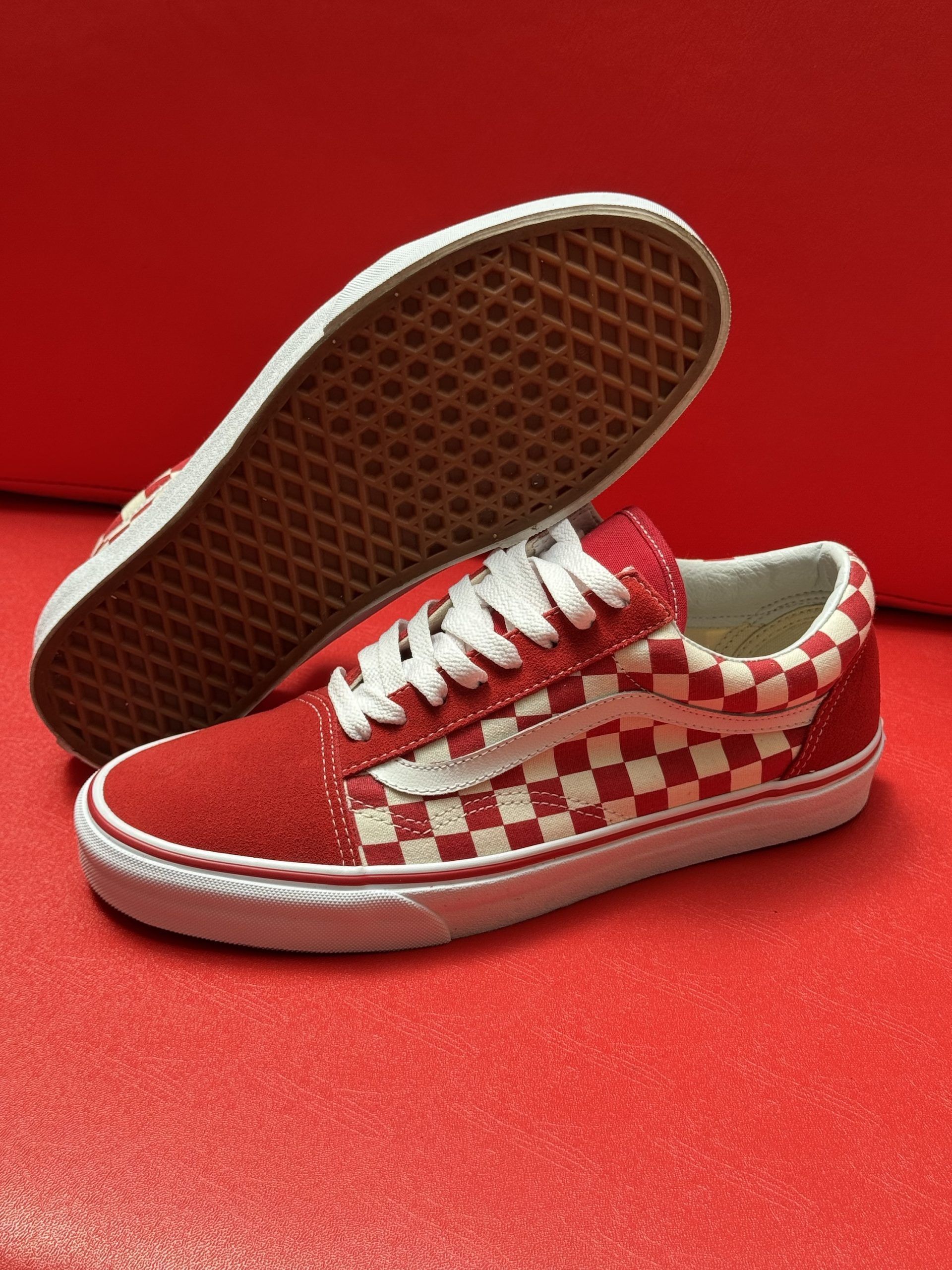 Red and white checkerboard Vans sneakers on a red surface.