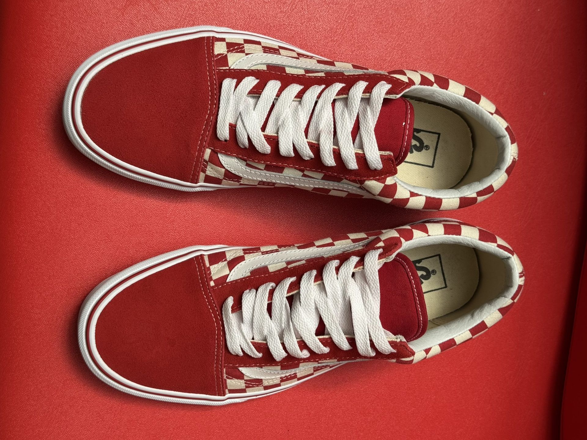 Red and white checkerboard Vans sneakers on a red surface.