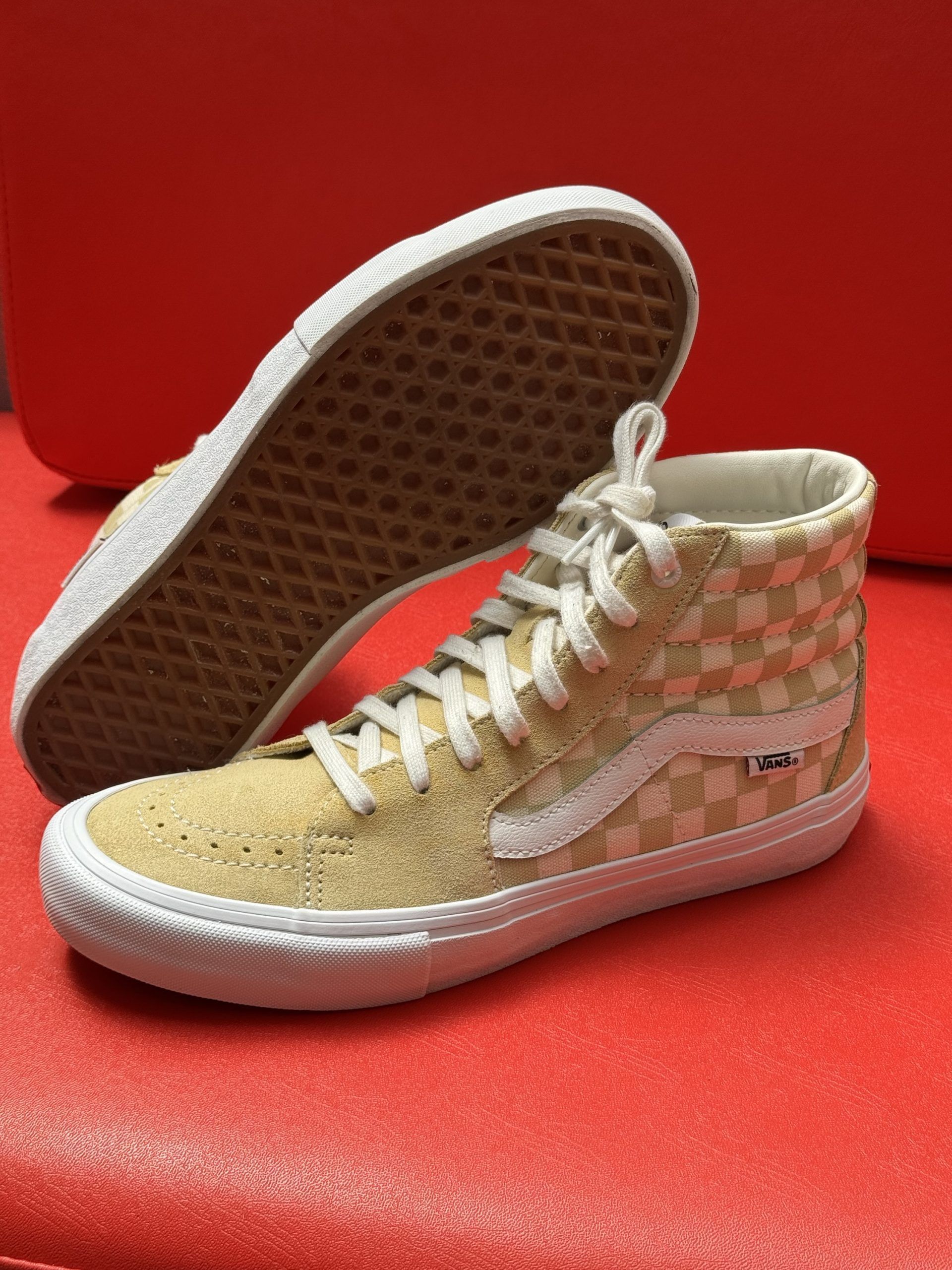 Tan Vans Sk8-Hi Pro sneakers with checkered pattern and white sole, set against a red background.