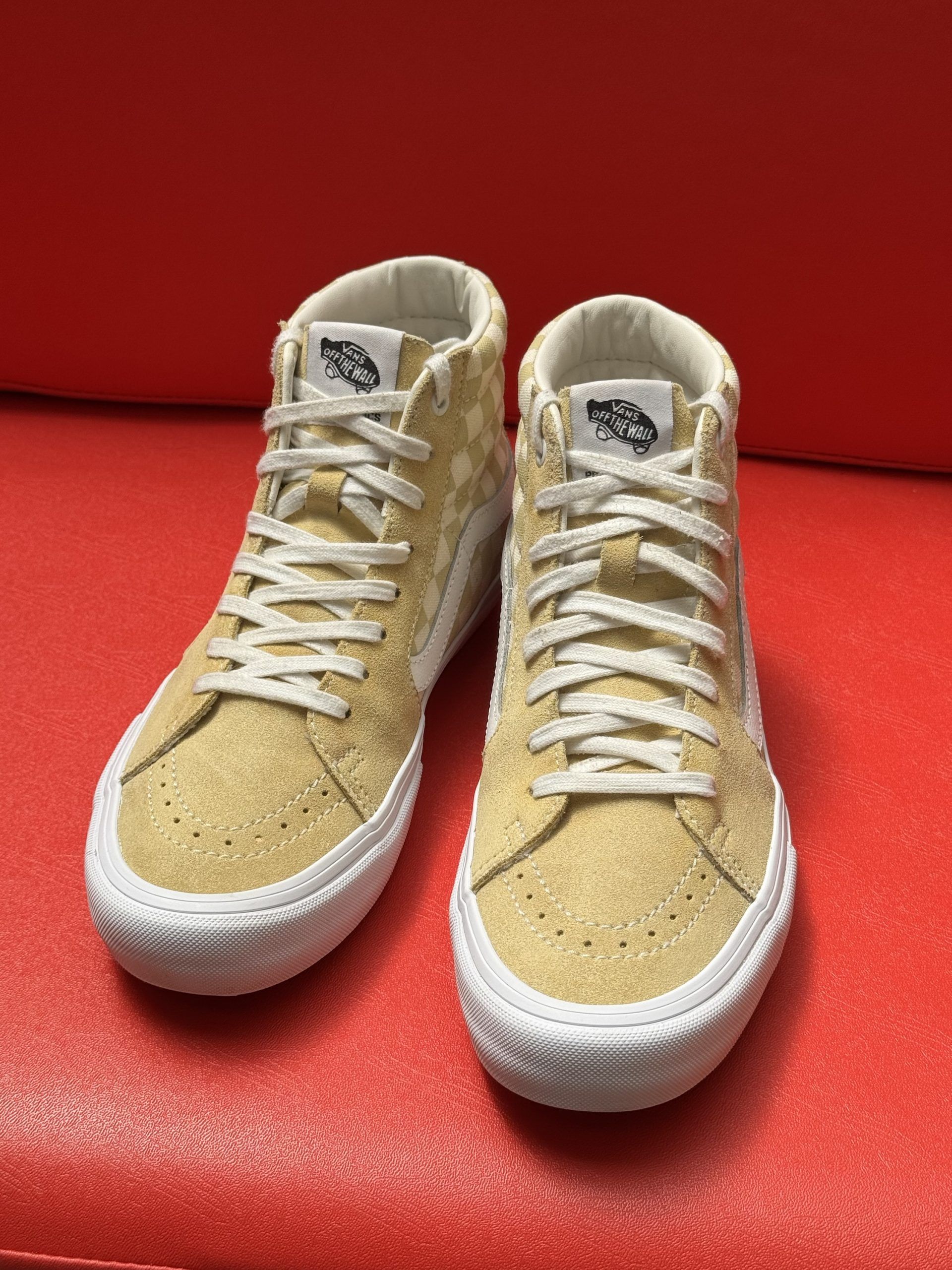 Tan Vans Sk8-Hi Pro sneakers with checkered pattern and white sole, set against a red background.