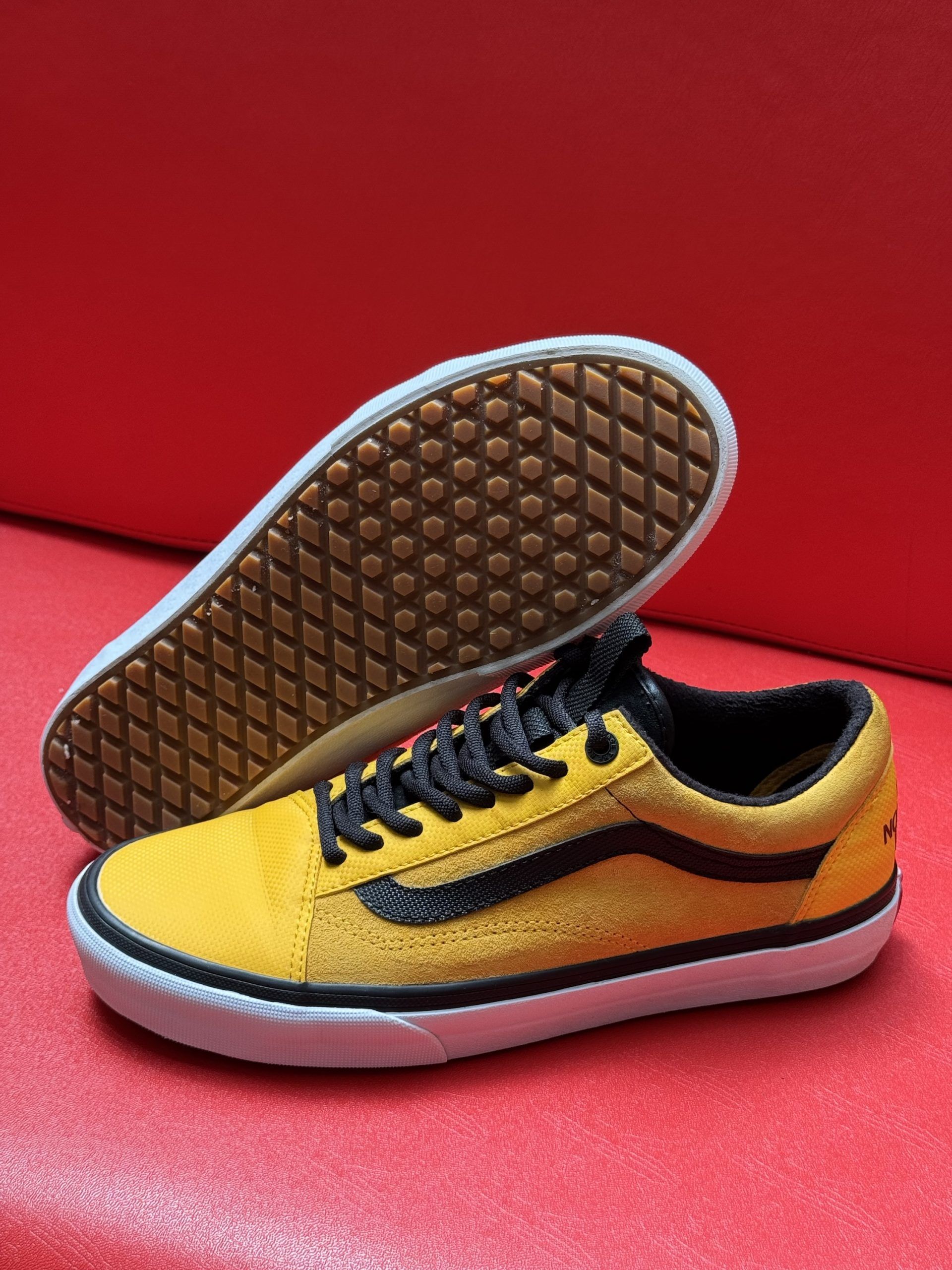 Yellow and black Vans Old Skool sneakers with a brown sole, on a red surface.