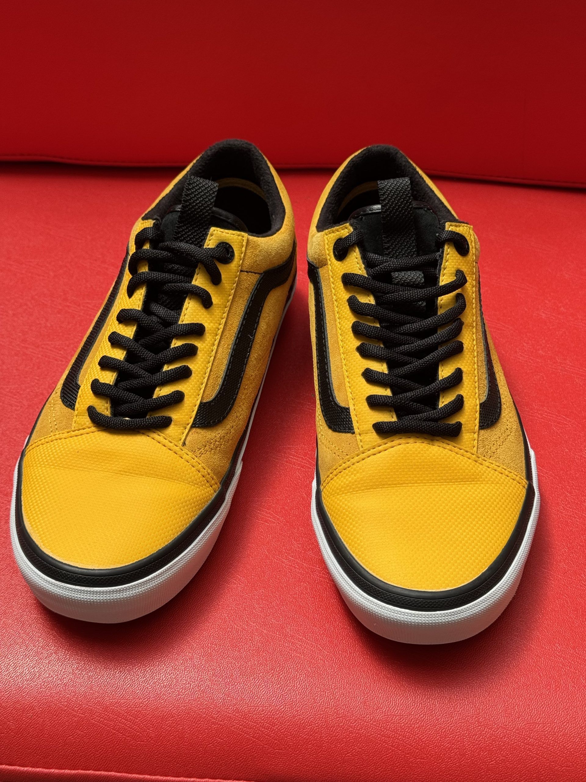 Yellow and black Vans Old Skool sneakers with a brown sole, on a red surface.