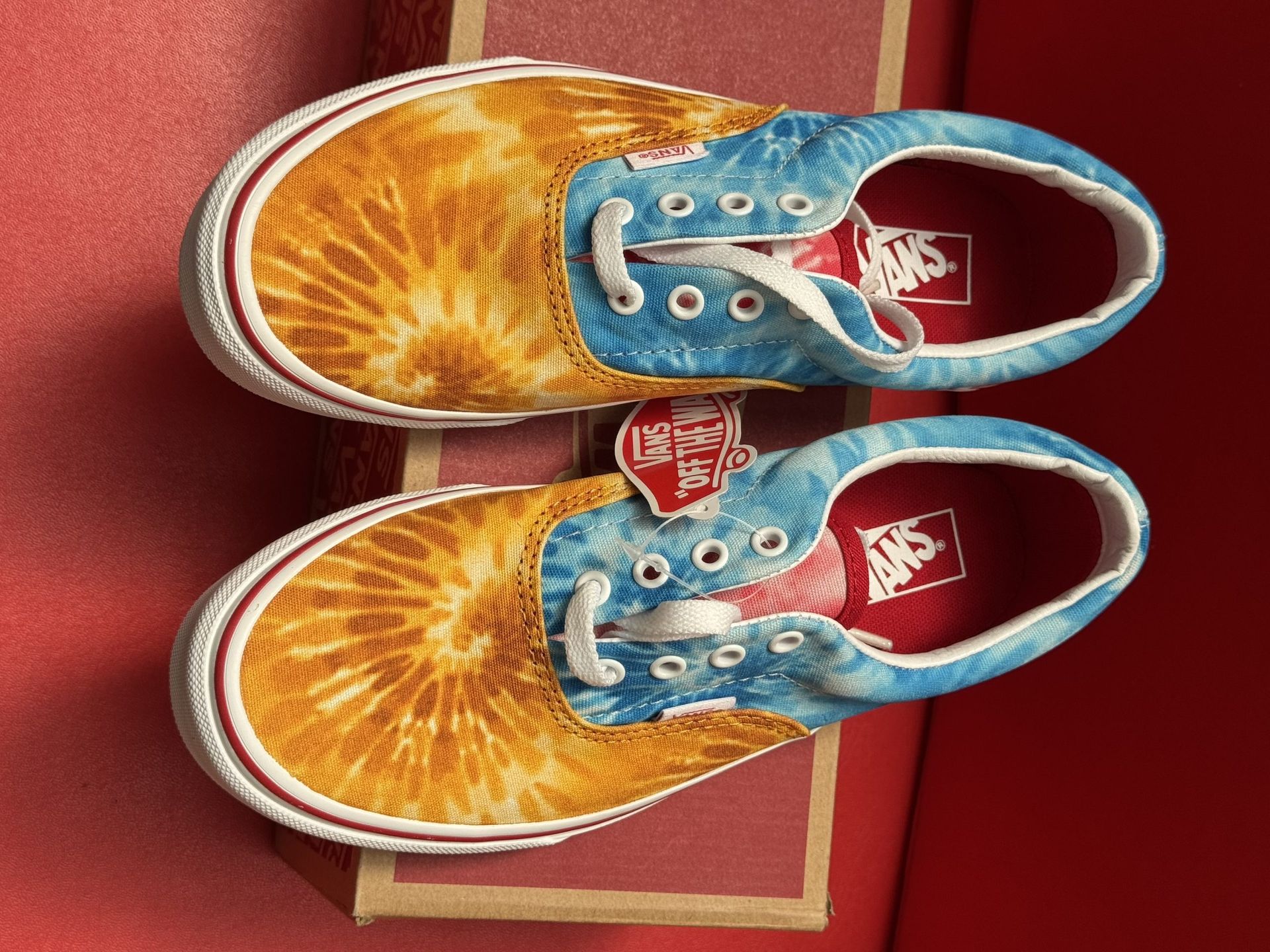 Vans sneakers in colorful tie-dye print on a box, with the sole visible. Red background.