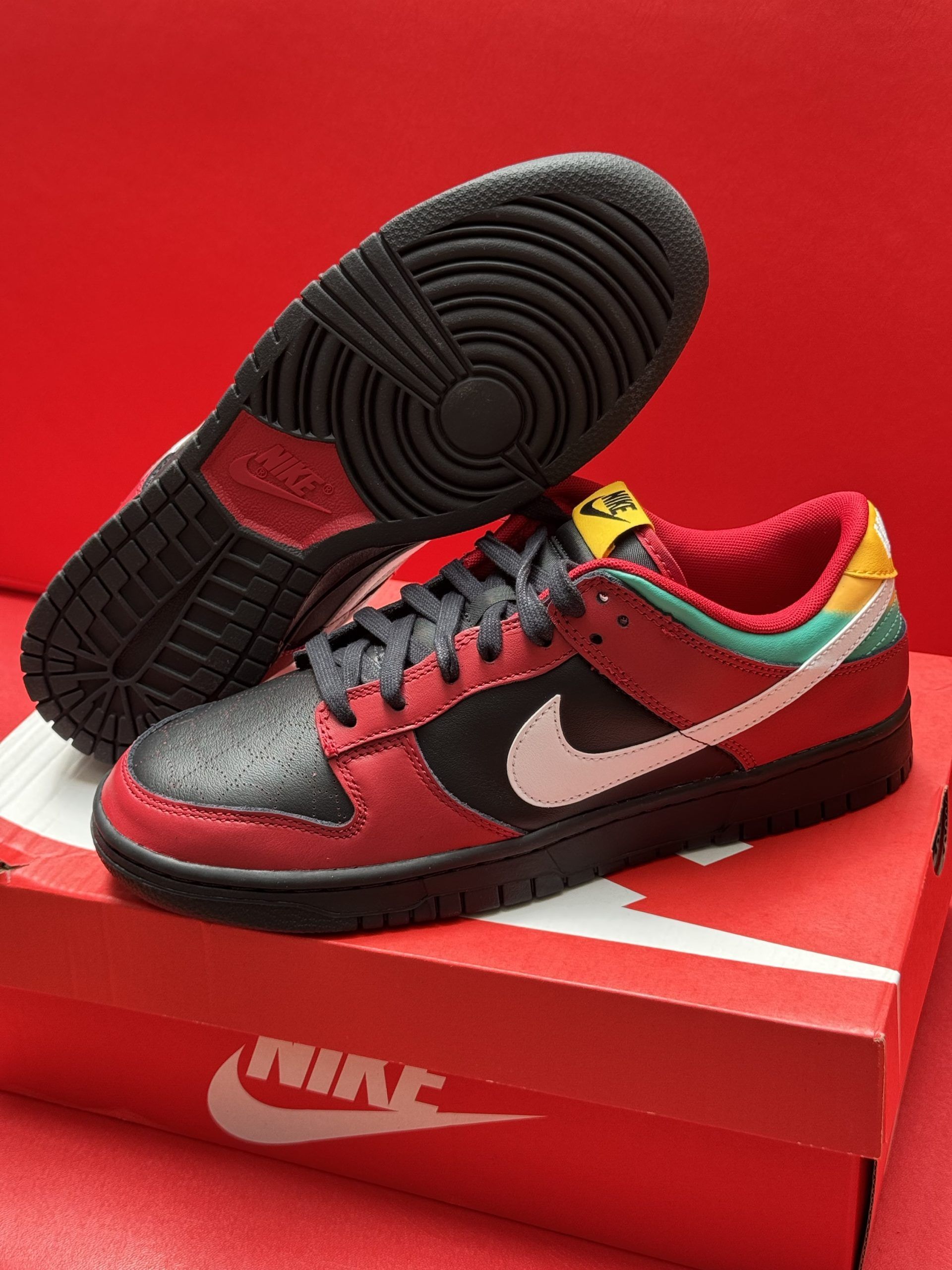 Red, black, white, and yellow Nike Dunk Low sneakers on a red Nike shoe box.
