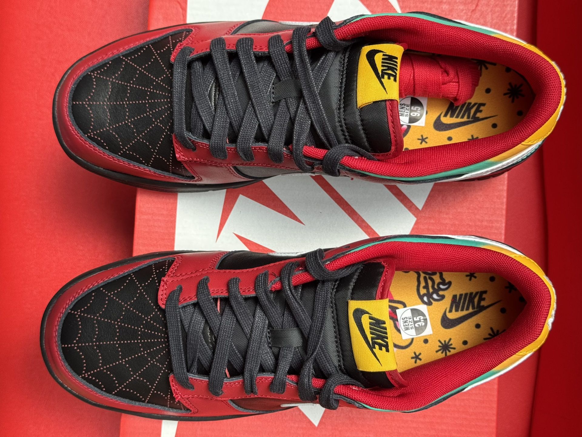 Red, black, white, and yellow Nike Dunk Low sneakers on a red Nike shoe box.