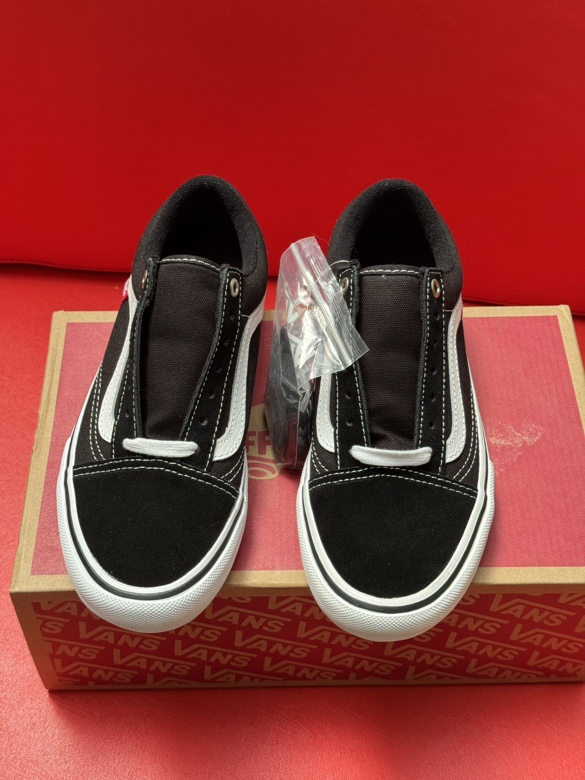 Black and white Vans sneakers on a box against a red backdrop. One shoe upside down showing the sole.