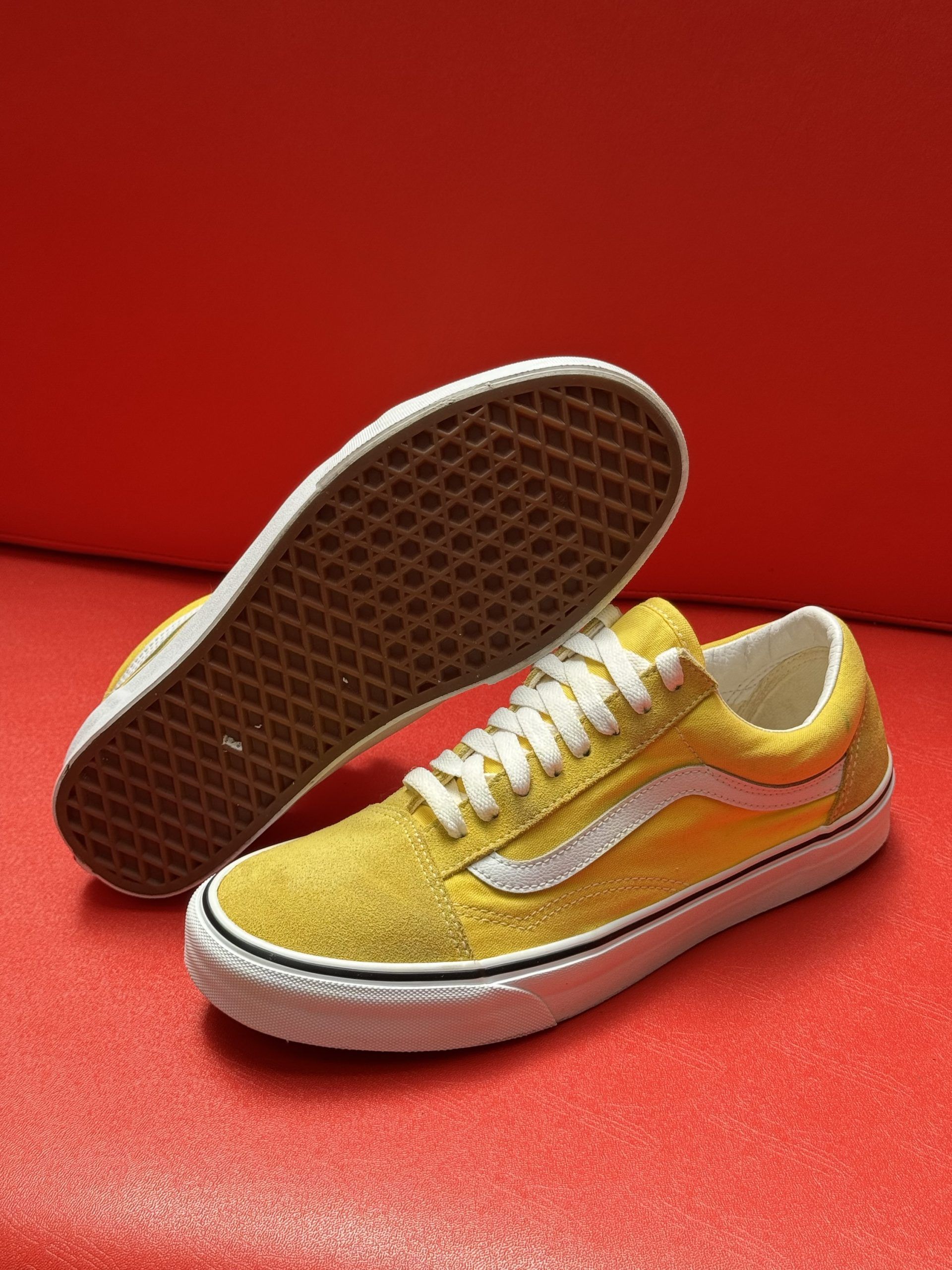 Yellow Vans sneakers with white stripe and sole, on a red surface.