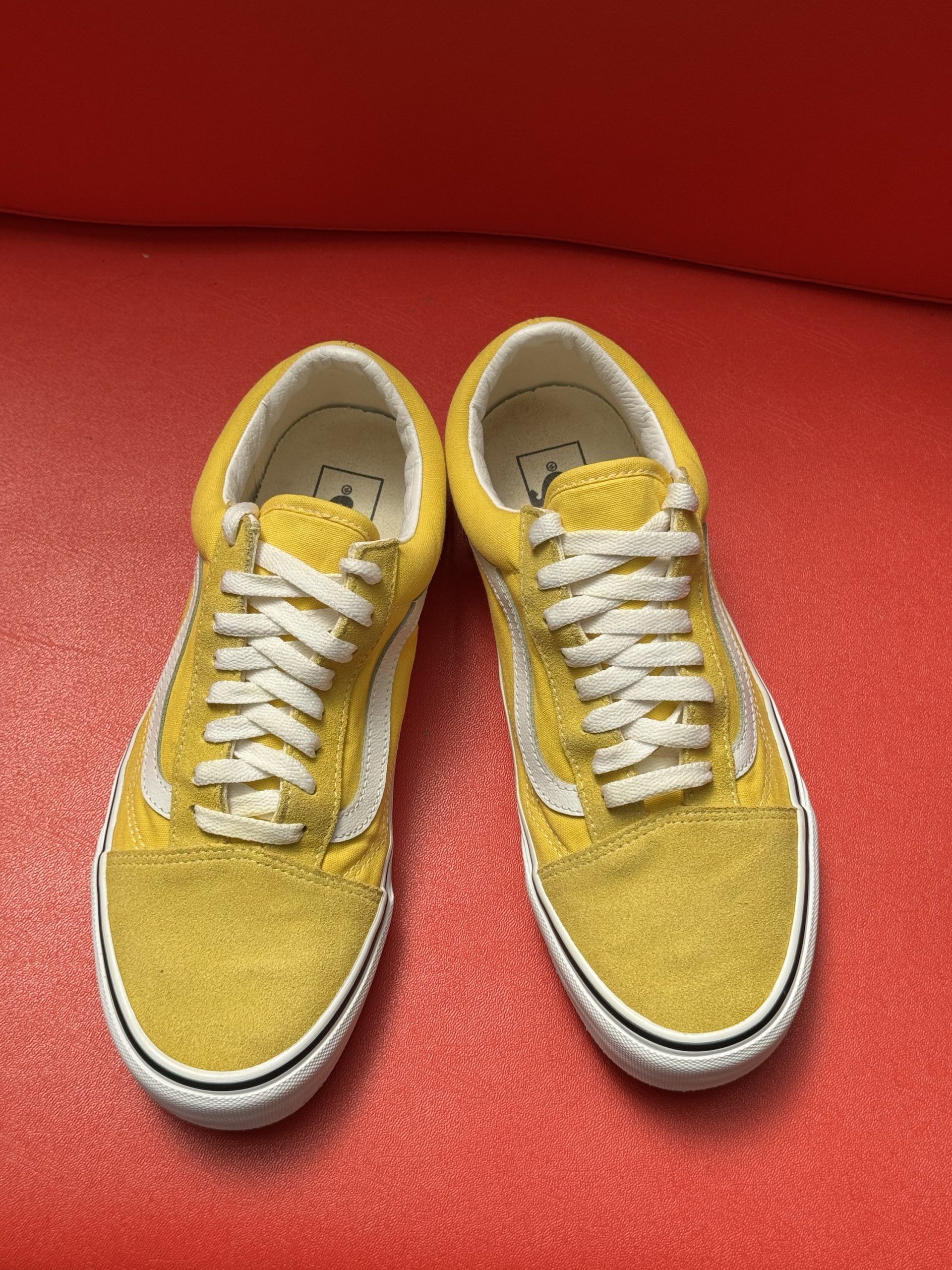 Yellow Vans sneakers with white stripe and sole, on a red surface.