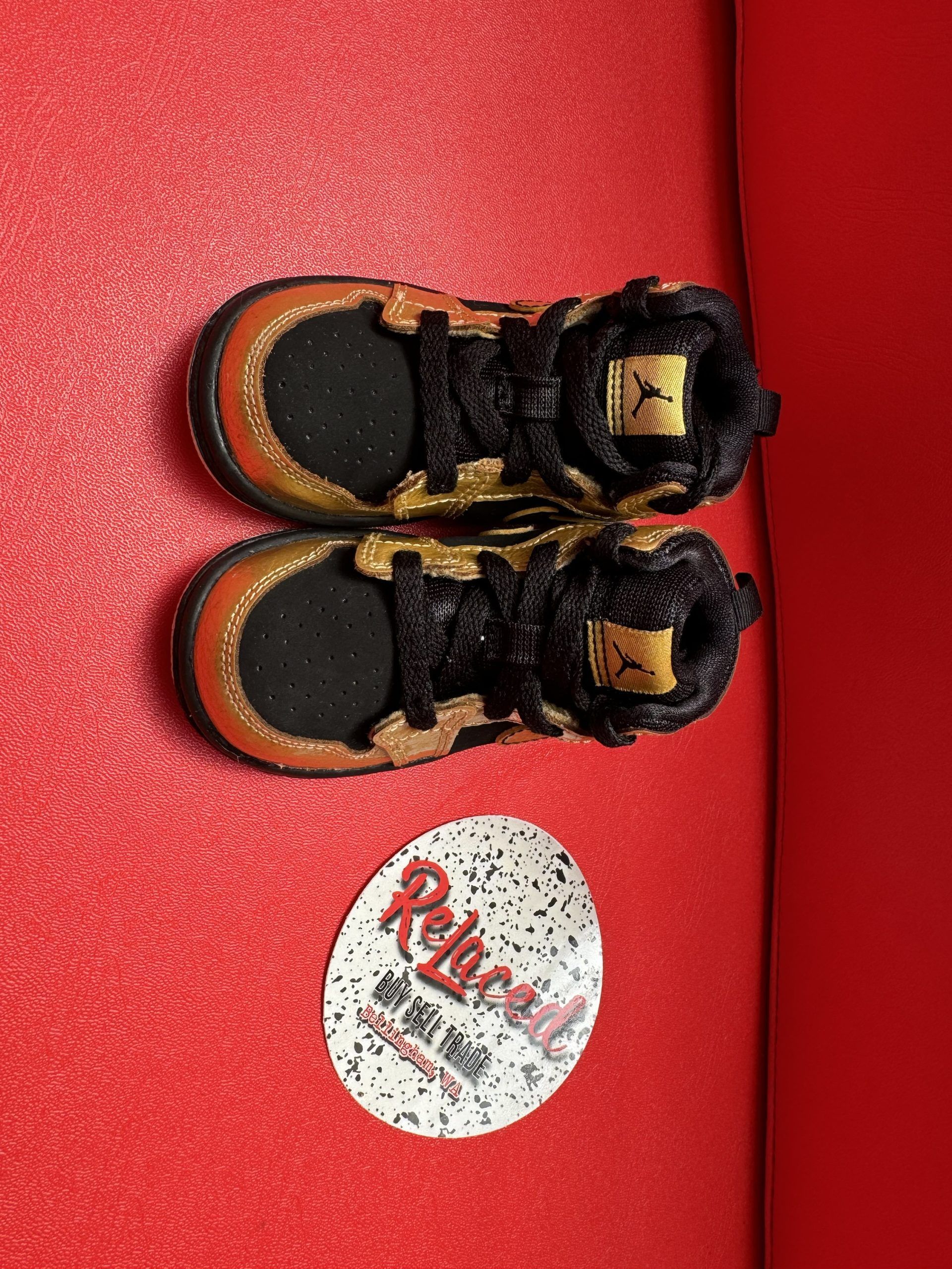 Gold and black baby Jordan sneaker with a red background, white sole is visible.