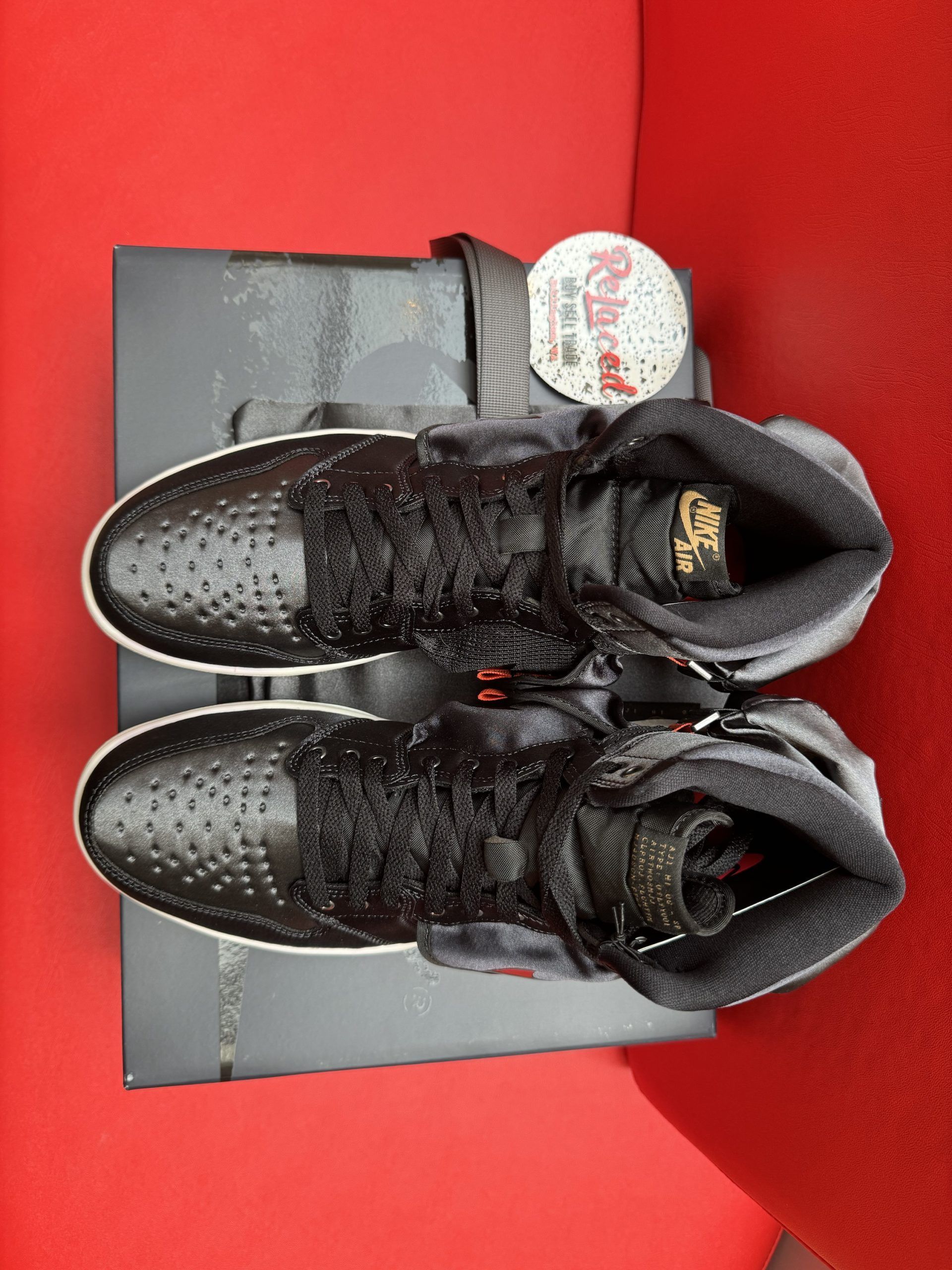 Black Air Jordan 1 sneaker on a box, with the sole facing up, on a red surface.