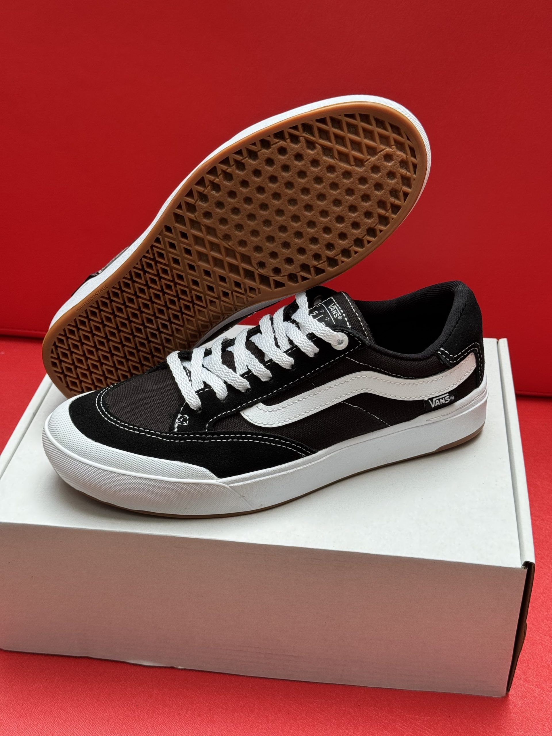 Black and white Vans sneakers with white sole, sitting on a white box, red background.