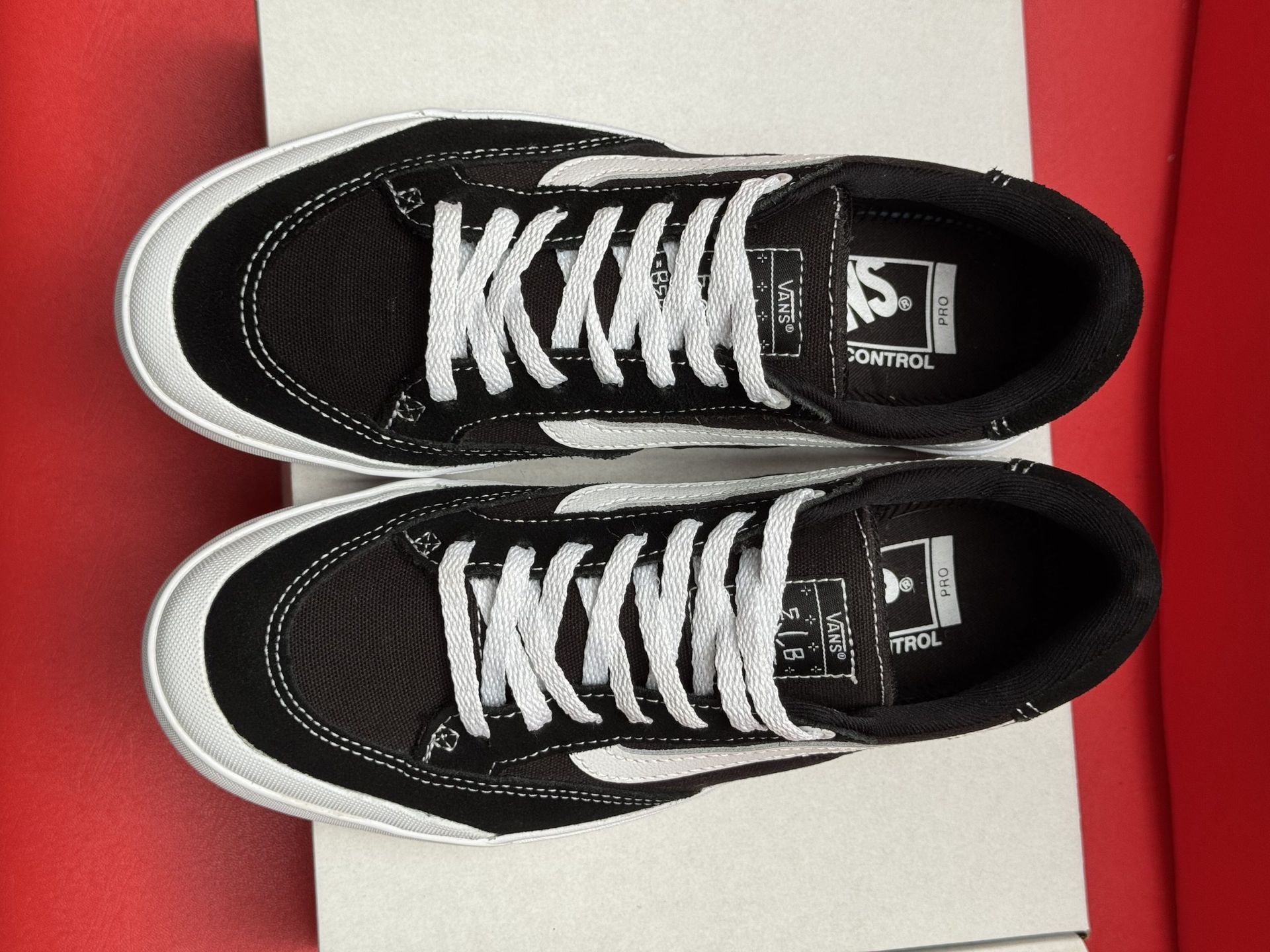 Black and white Vans sneakers with white sole, sitting on a white box, red background.