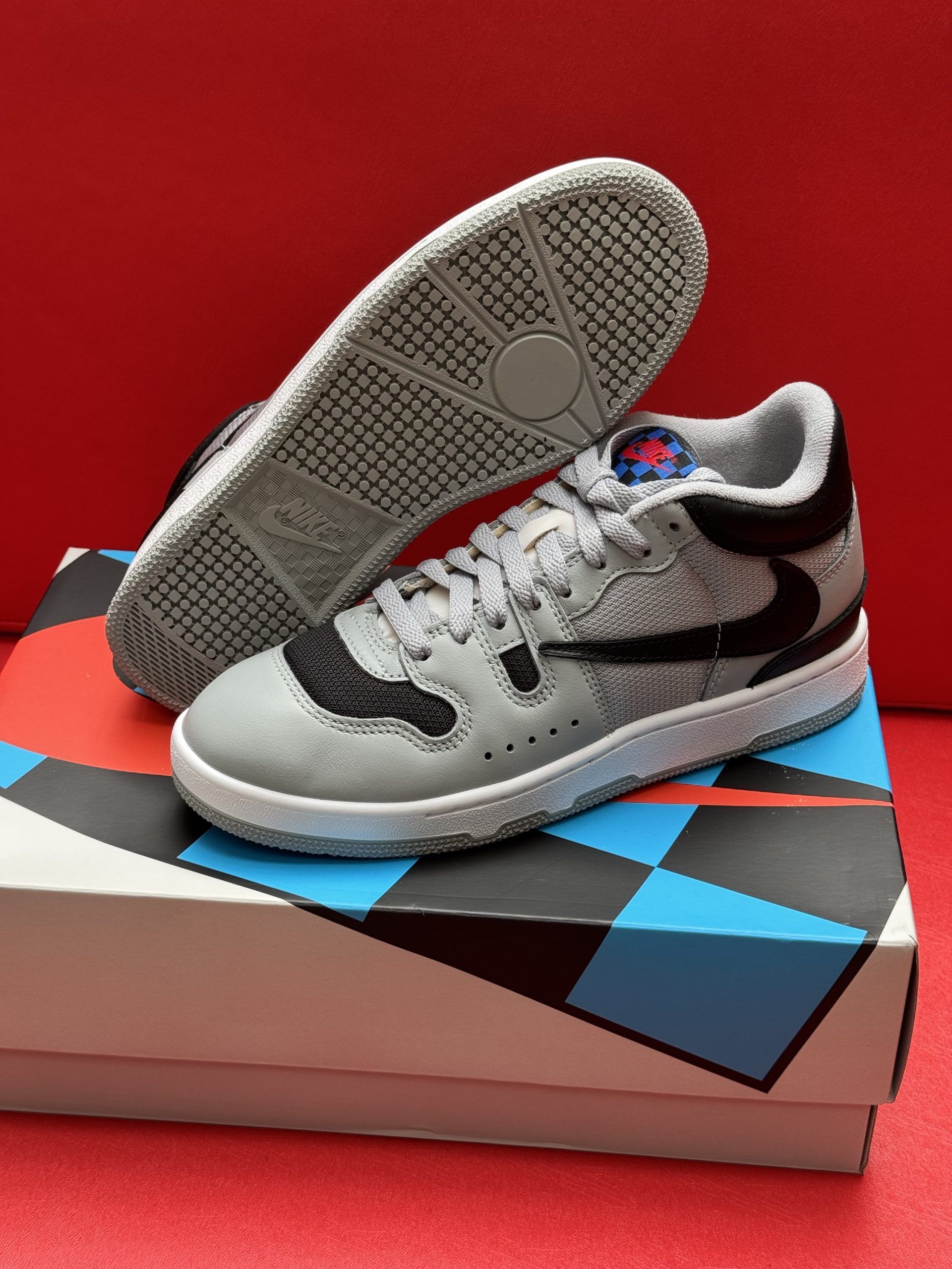 Gray and black sneakers with blue accents on a patterned box against a red background.