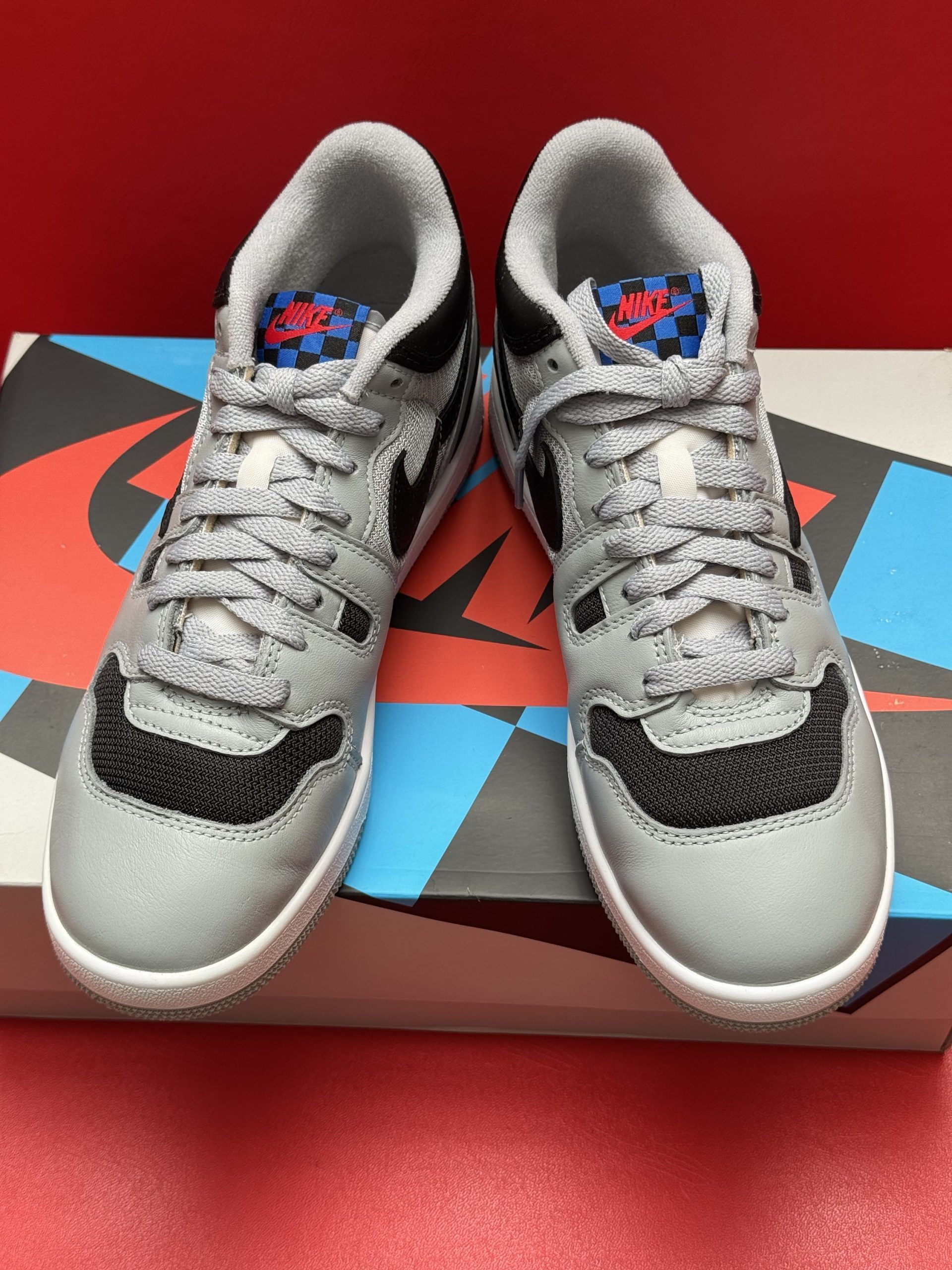 Gray and black sneakers with blue accents on a patterned box against a red background.