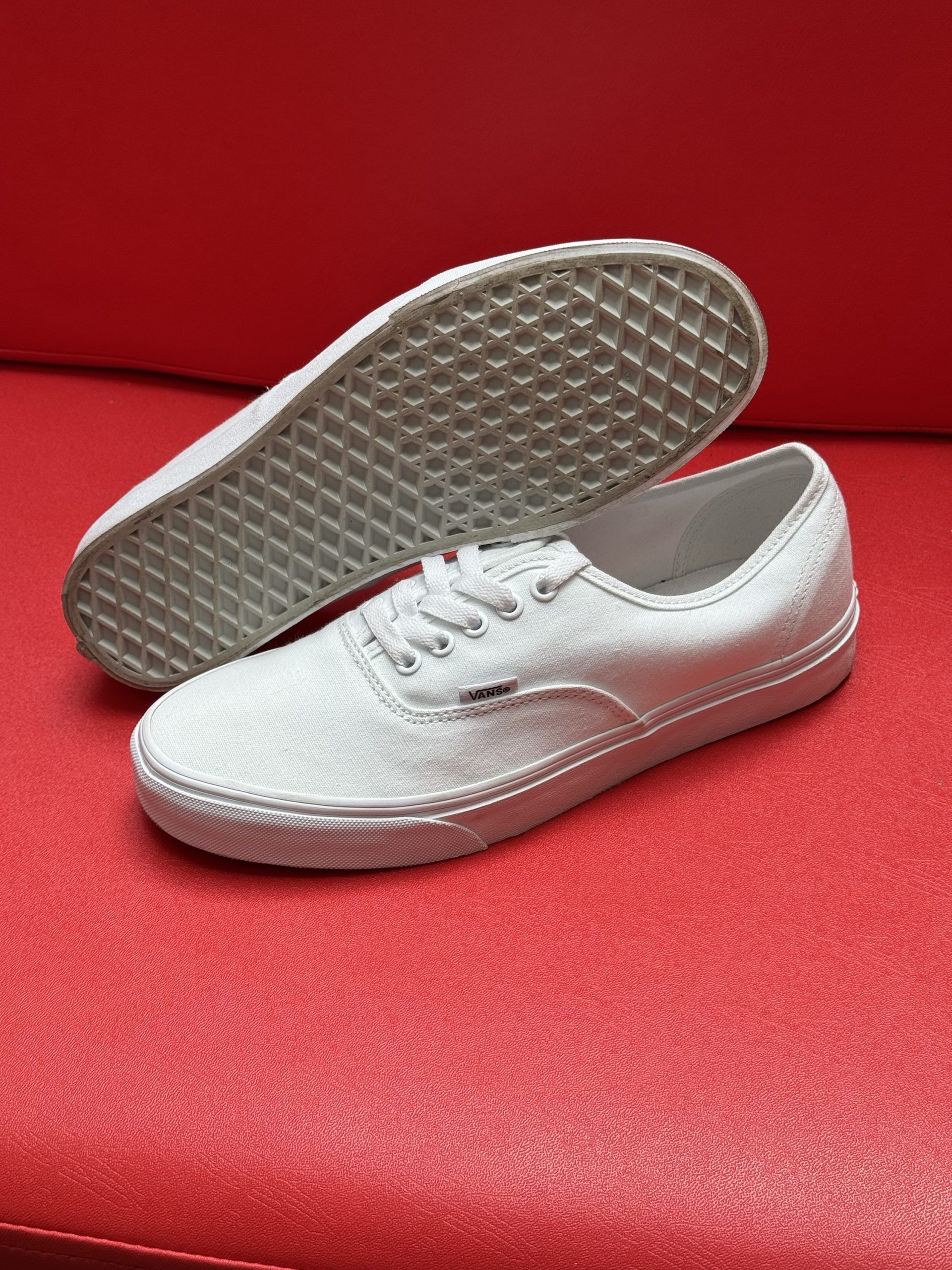 White canvas sneakers on a red surface, one shoe turned to show the sole.