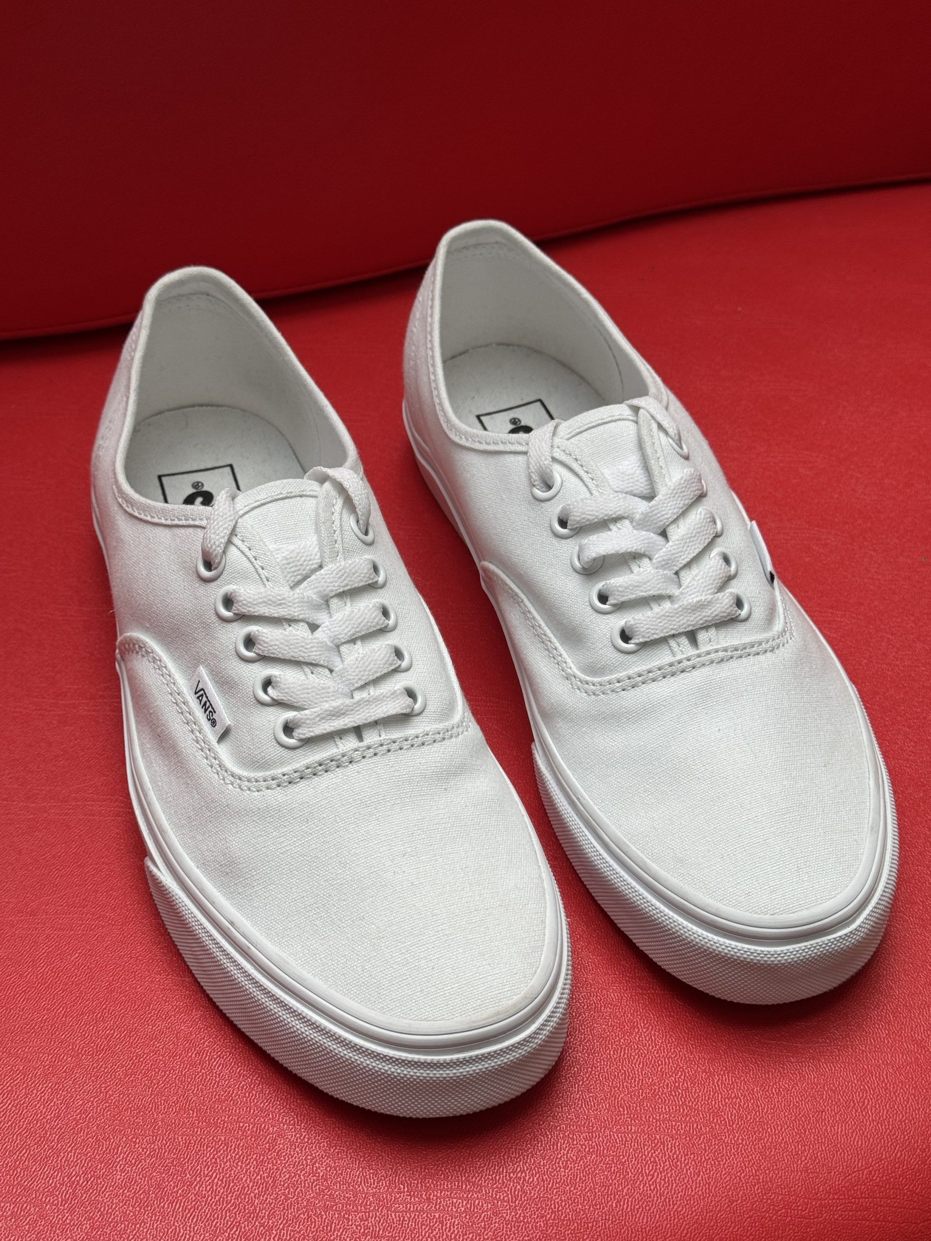 White canvas sneakers on a red surface, one shoe turned to show the sole.