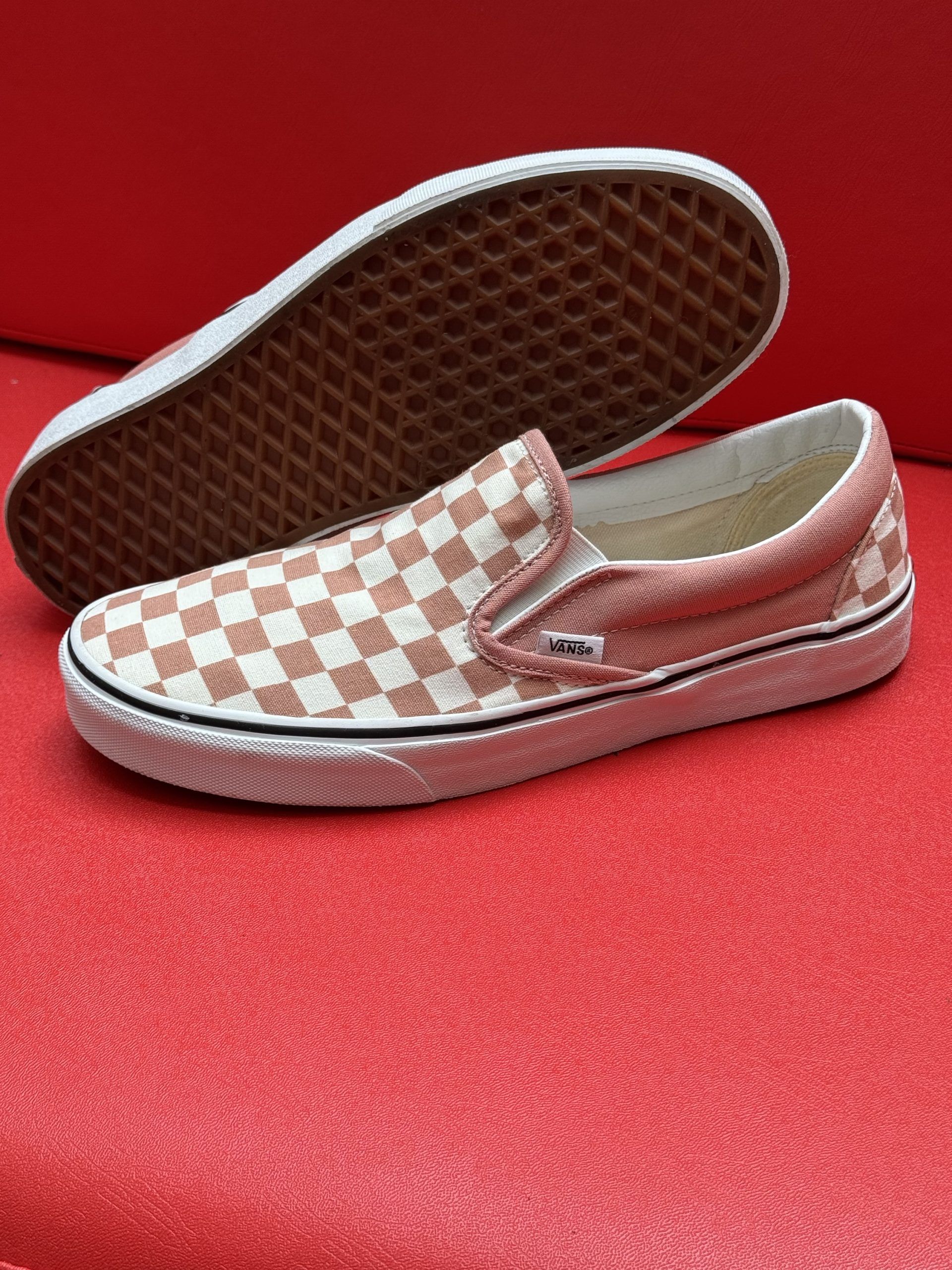 Checkered slip-on sneakers in white and pink, with white soles, on a red surface.