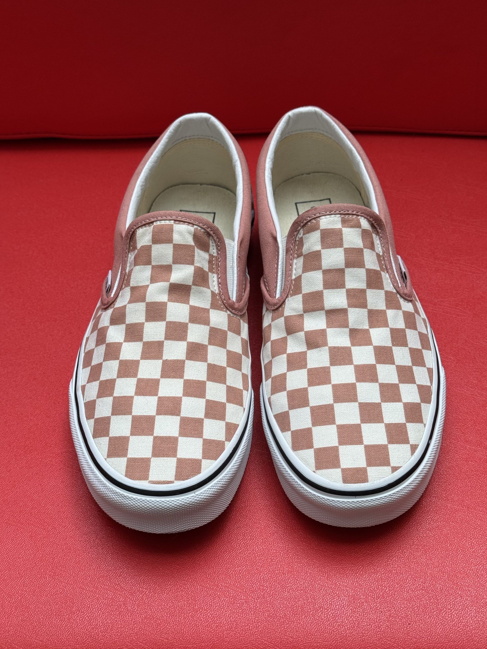 Checkered slip-on sneakers in white and pink, with white soles, on a red surface.