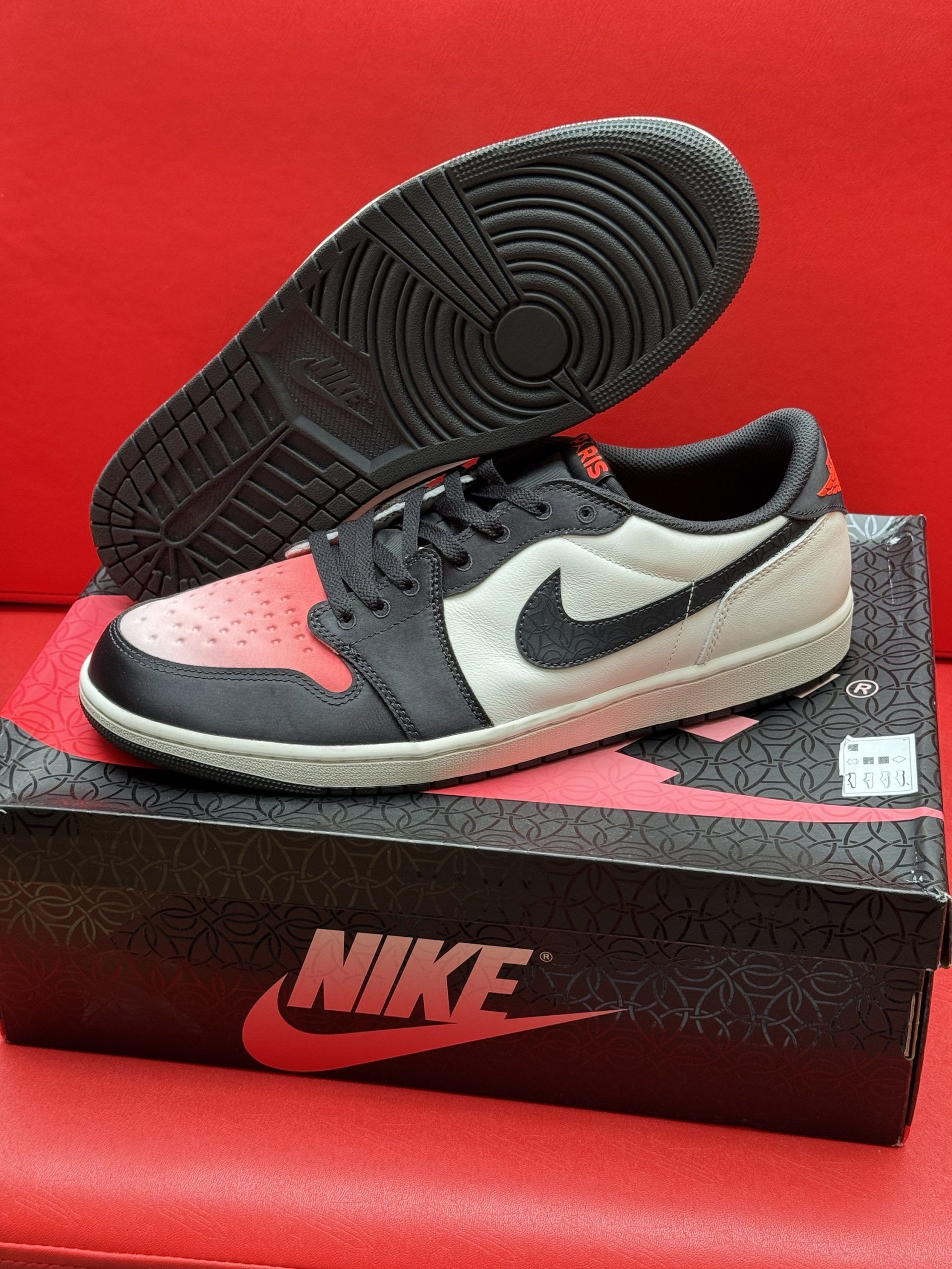 Black, red, and white Air Jordan 1 Low sneaker sits on a black shoe box. The sole is visible.